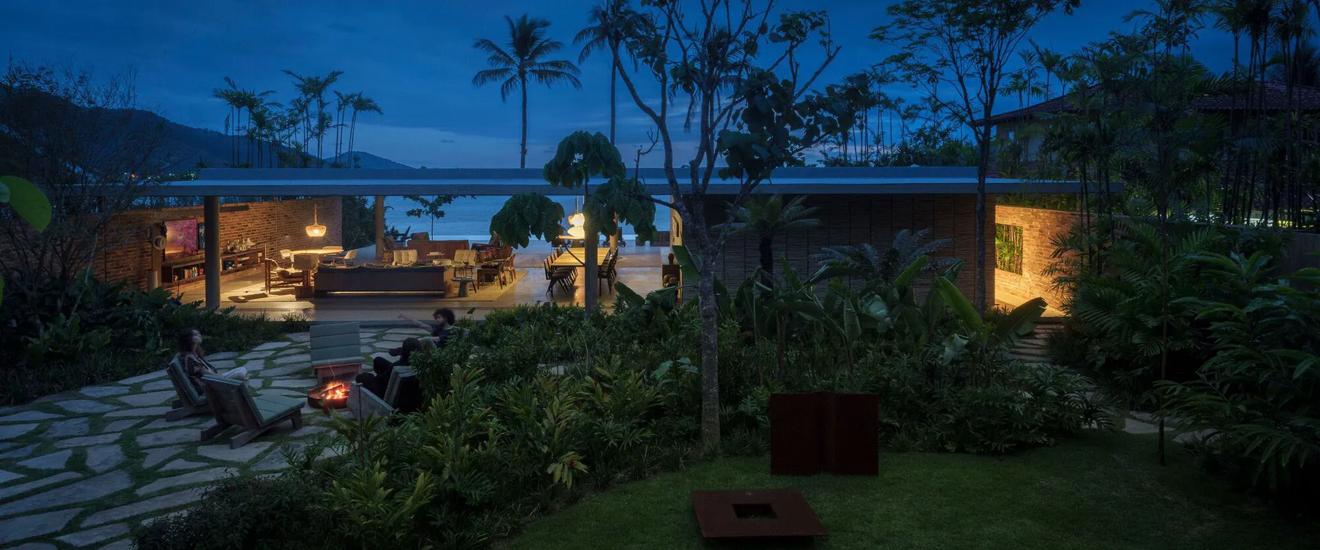 Vacation home exterior with concrete materials and tropical landscaping at night.