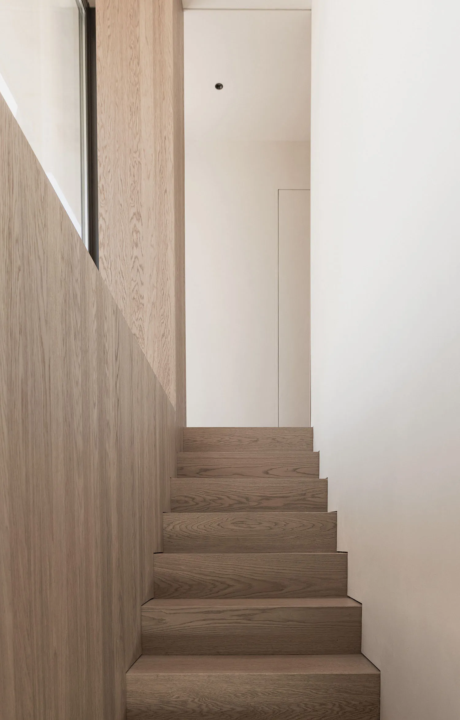 Modern minimalist staircase with wooden steps and light-colored walls.