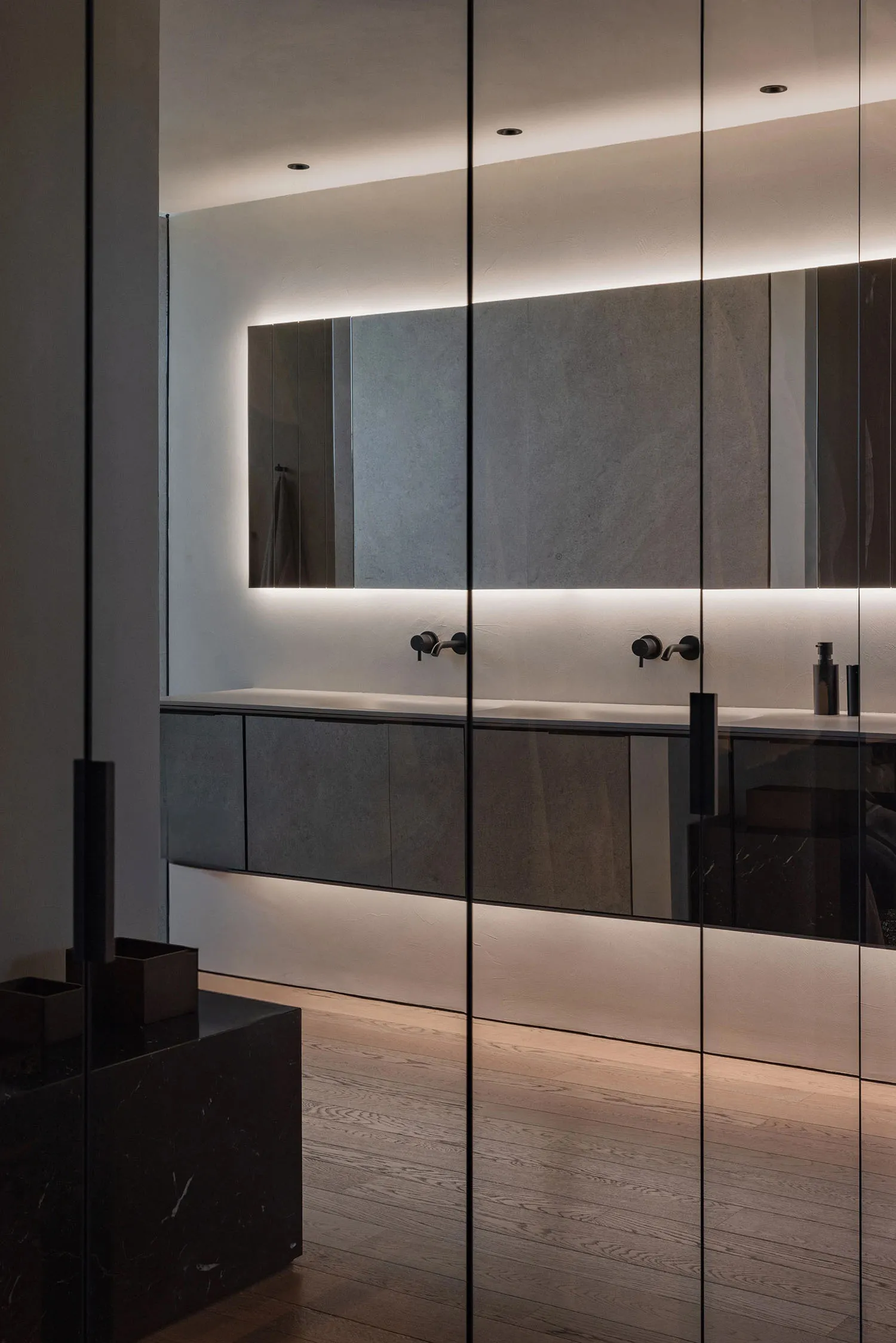 Modern bathroom interior featuring concrete countertops, glass wall, and wooden floor.