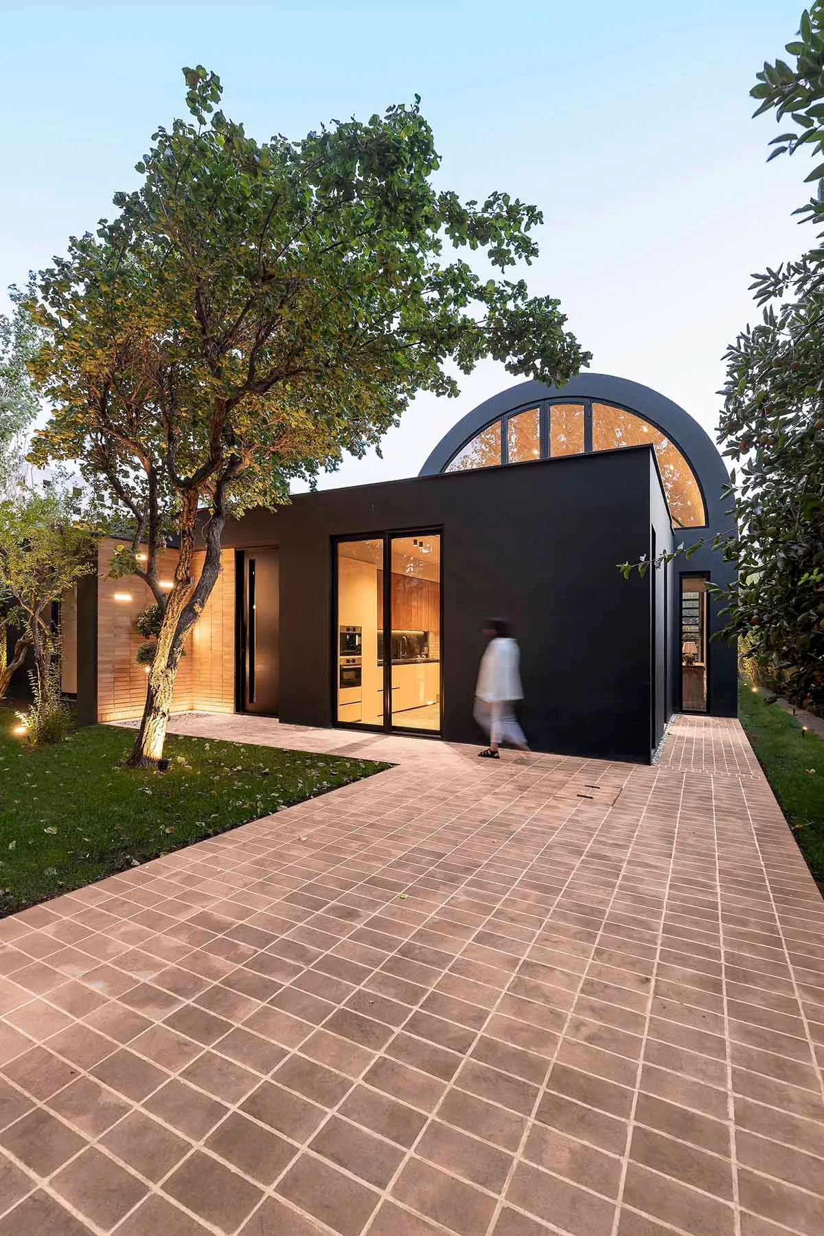 A modern residential house with a black exterior and large windows, surrounded by greenery.