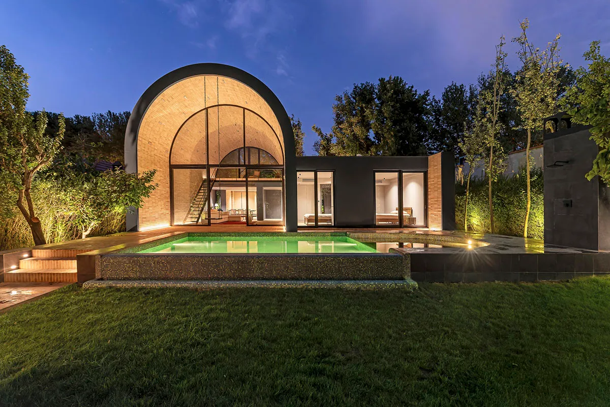 Modern residential architecture featuring an arched entrance and a swimming pool illuminated at night.
