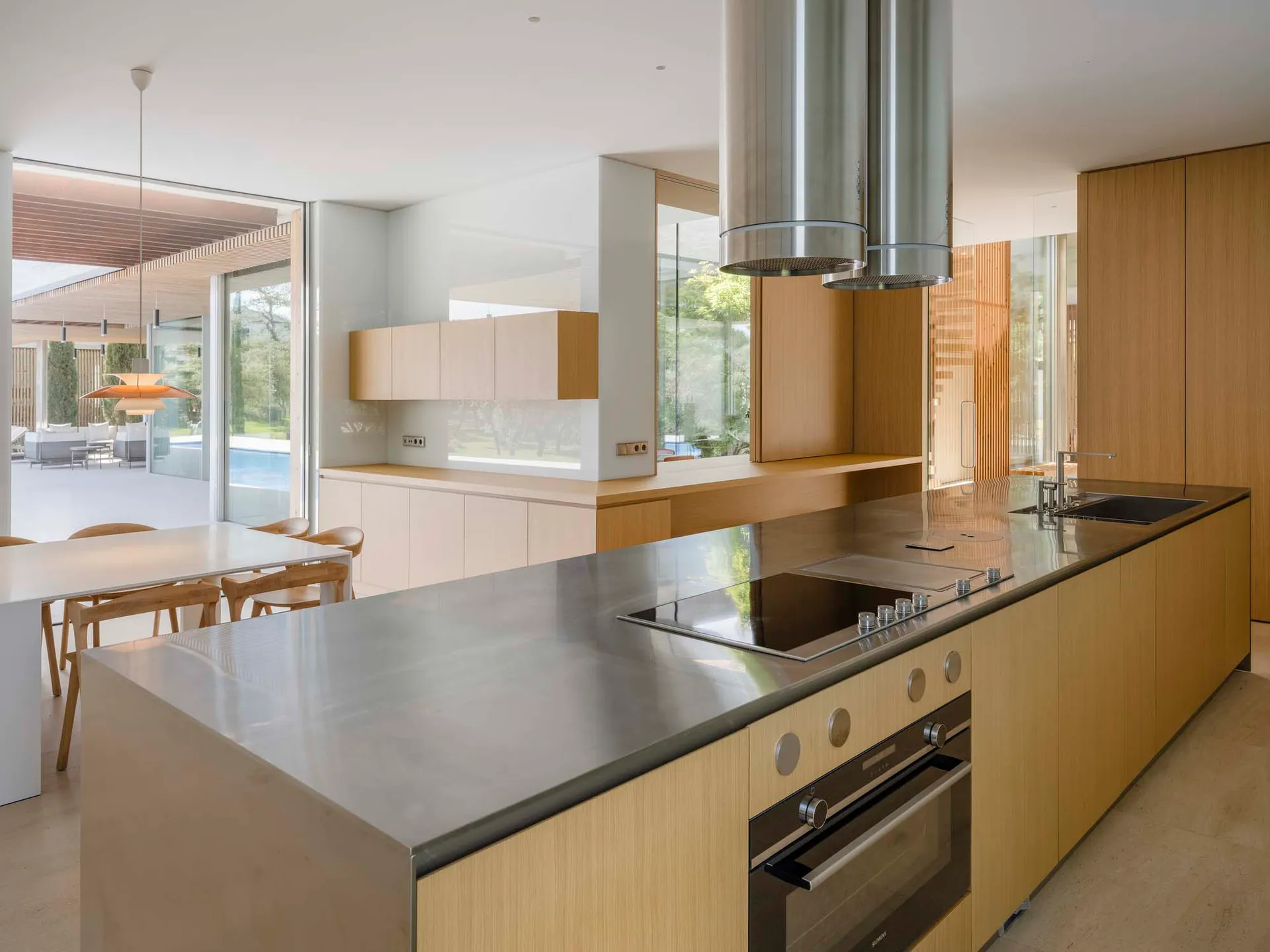 Modern, residential kitchen with wood cabinetry, stainless steel countertops, and glass backsplash.