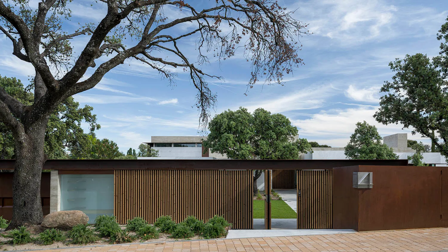A modern residential exterior with a metal fence and rustic tree.