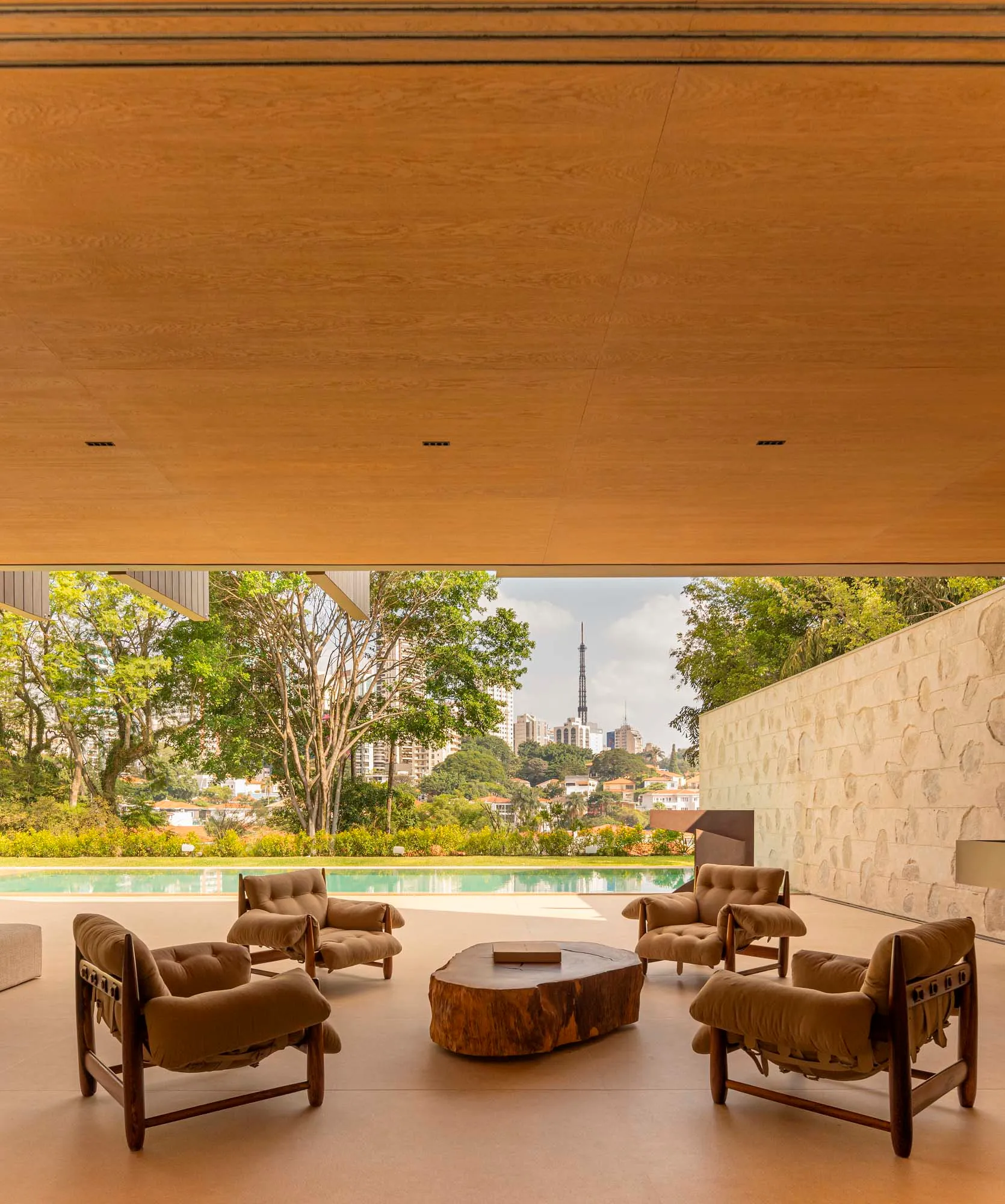 Modern minimalist living room with a wood floor and a large glass wall overlooking a pool and cityscape.
