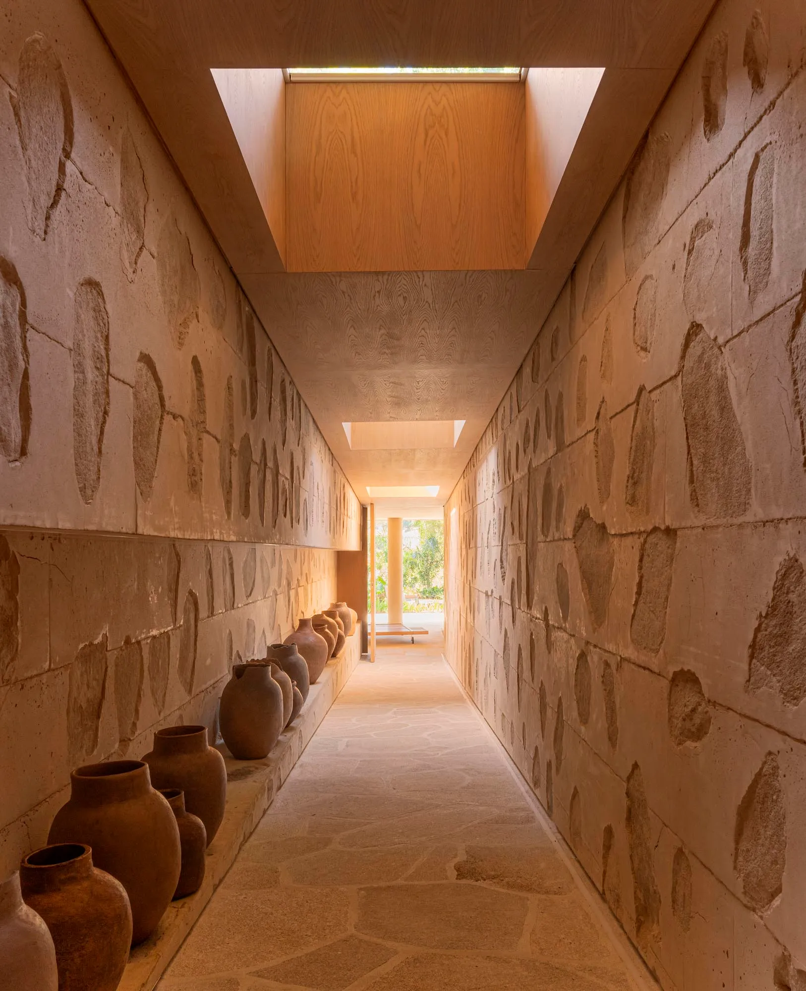 A hallway lined with clay vases, featuring a skylight.