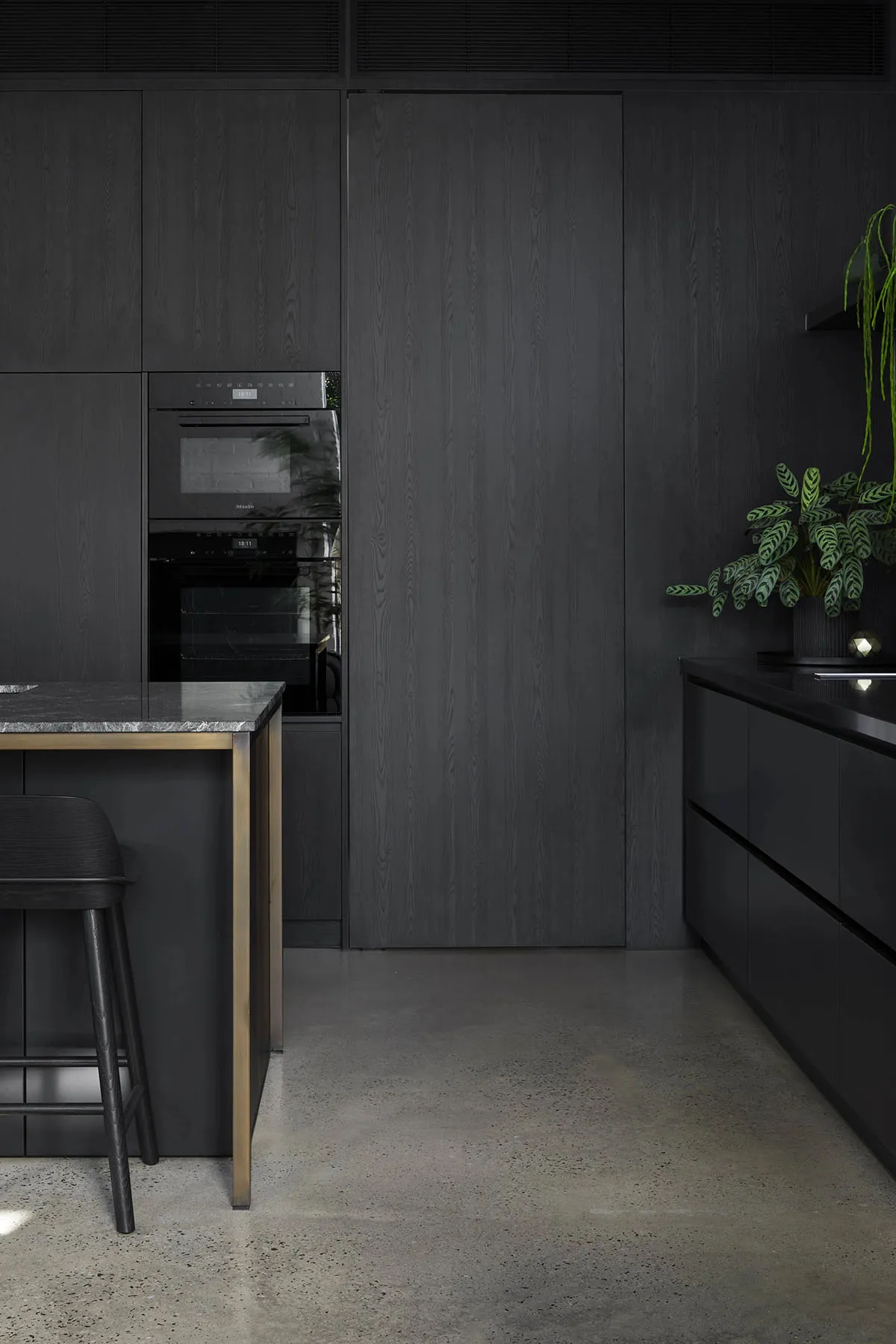 A modern kitchen with black wooden cabinets and a marble countertop.