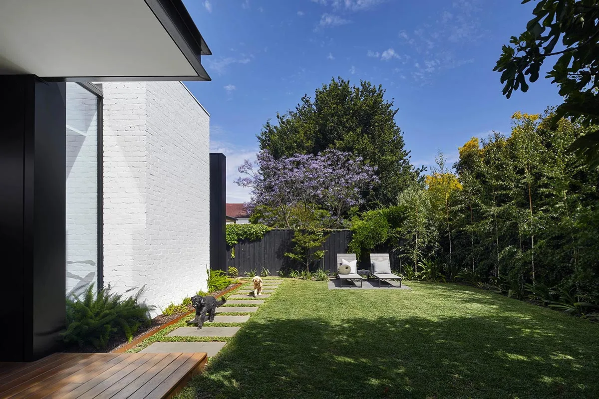 A modern house exterior with a concrete pathway and a brick wall in the backyard.