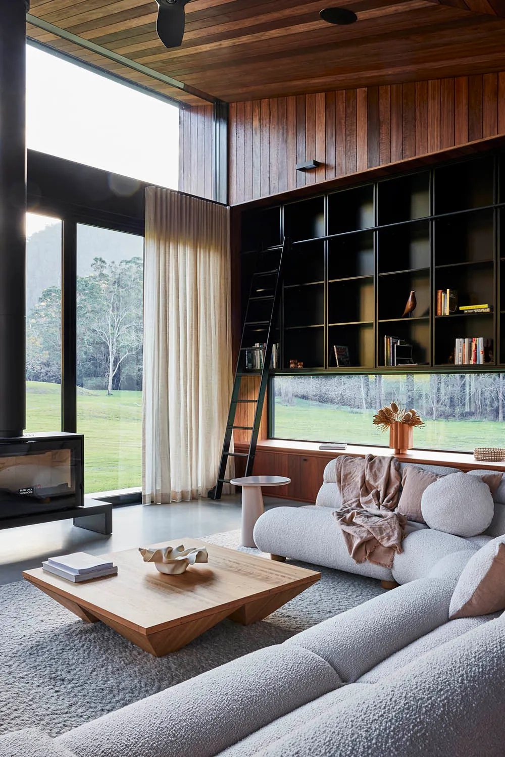 A modern living room with large windows, a wooden coffee table, and a comfortable sofa.