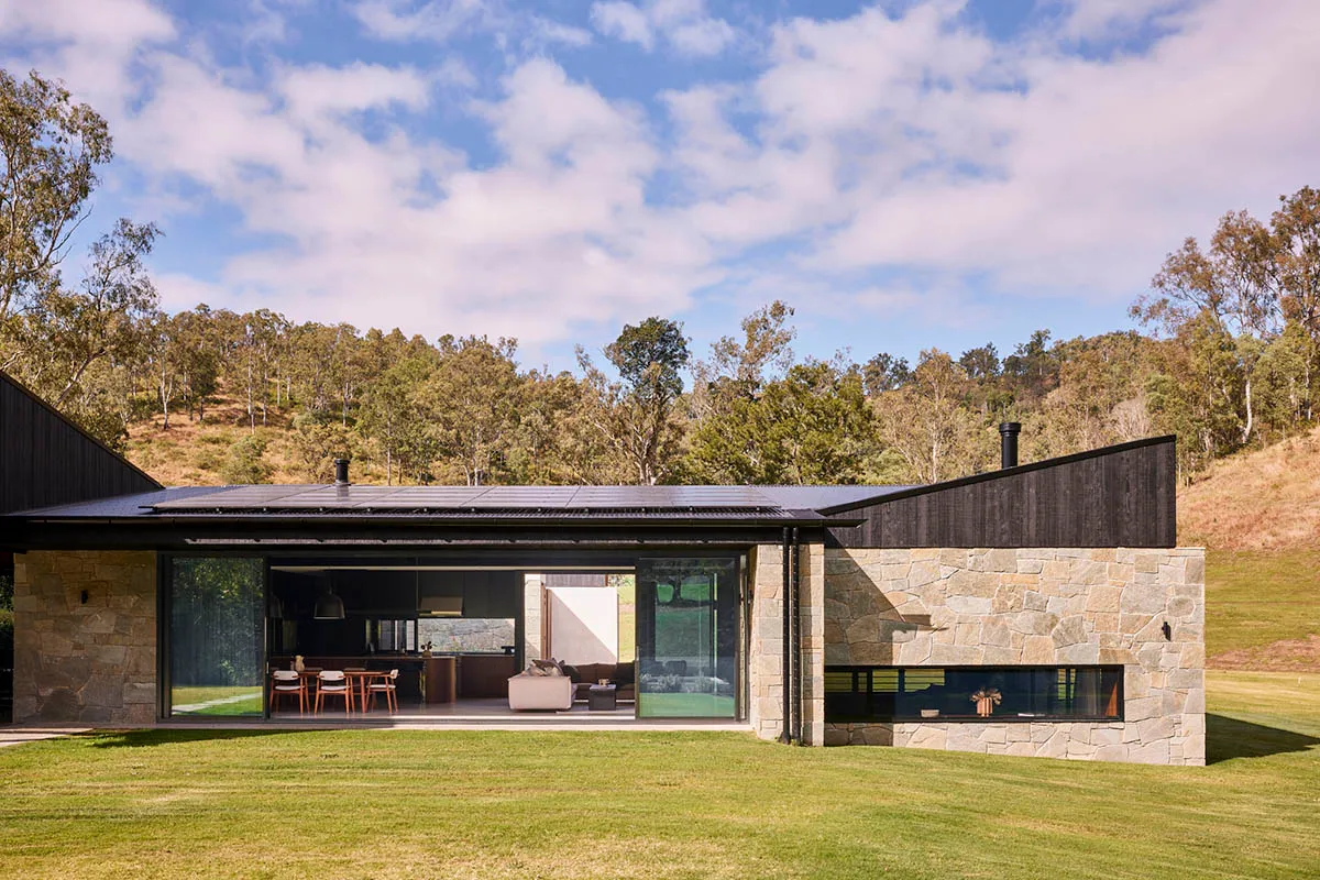 Modern residential building with stone and glass exterior, featuring expansive windows and a spacious outdoor area.