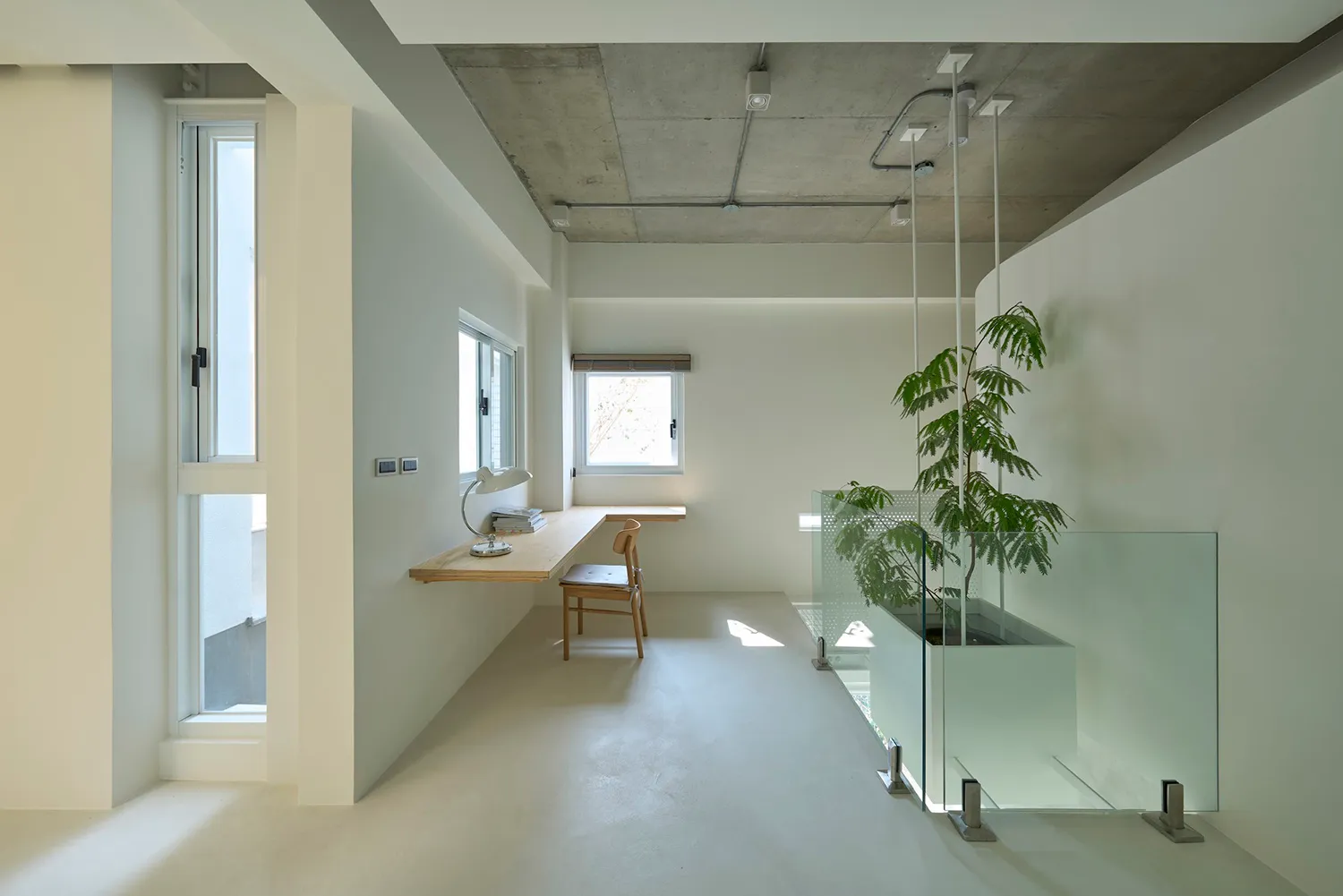 A minimalist home office with concrete and glass elements, featuring a desk, chair, and window.