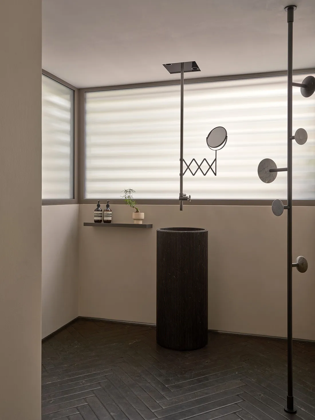 Modern minimalist bathroom featuring a concrete pedestal sink, a black metal pole with a small circular mirror, and a herring