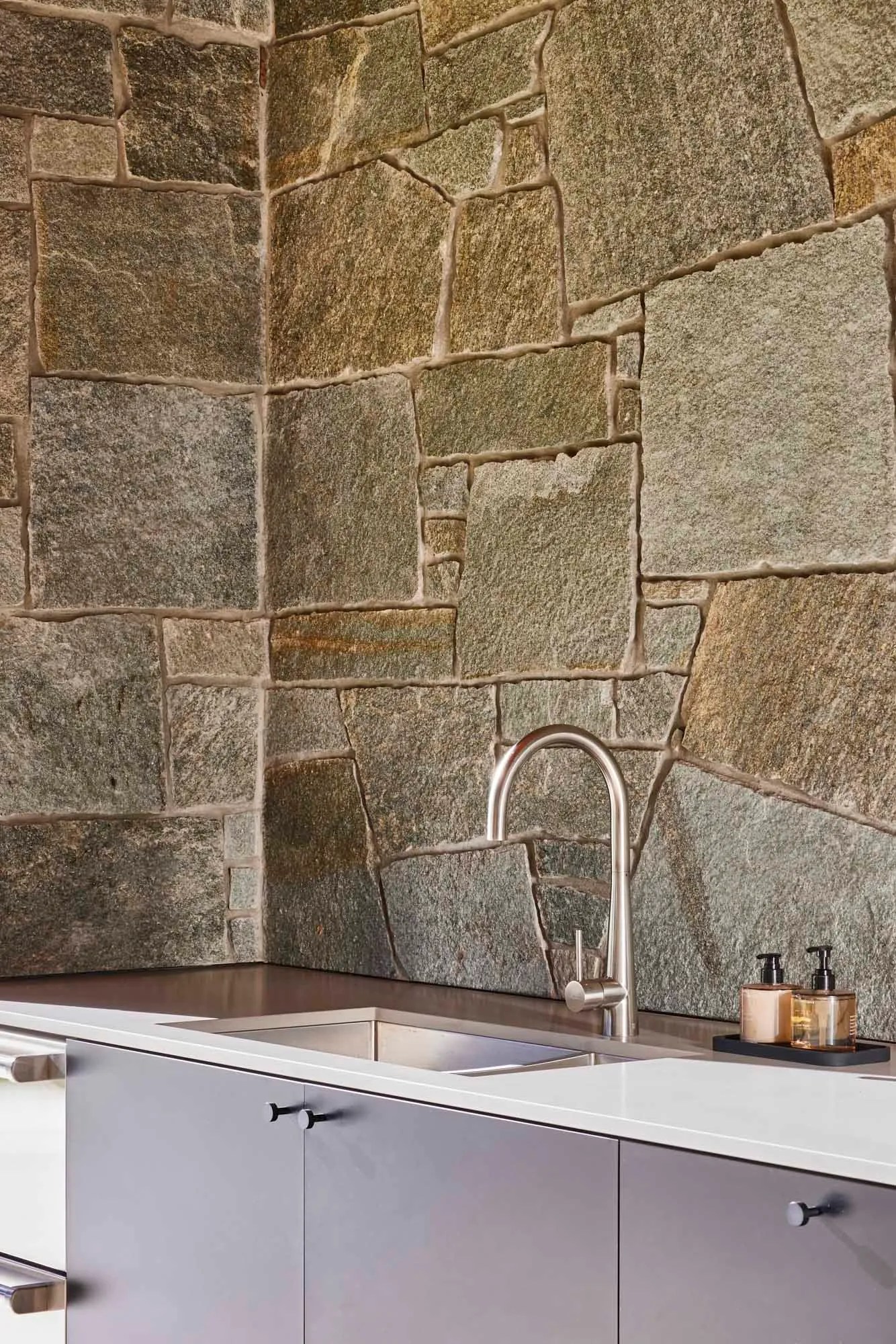 A modern kitchen with a stone wall and stainless steel faucet