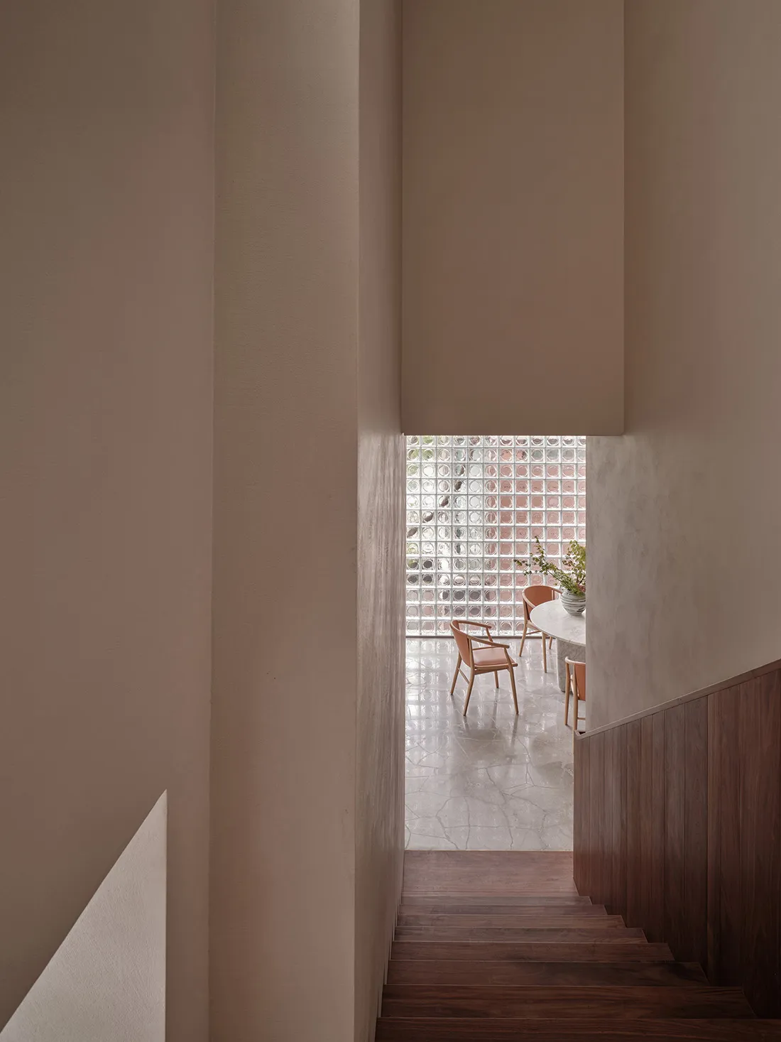A modern living room with wooden stairs and a cement floor, featuring a clear glass partition and natural light.