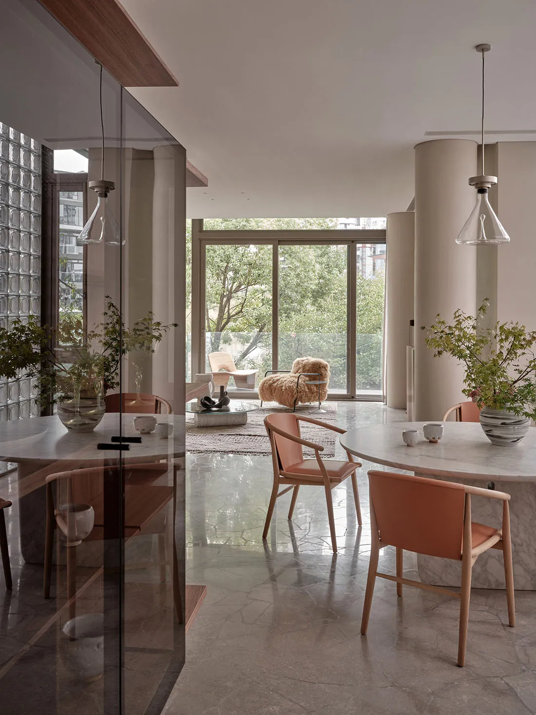 Modern, minimalist kitchen with marble countertops, wooden chairs, and large windows.