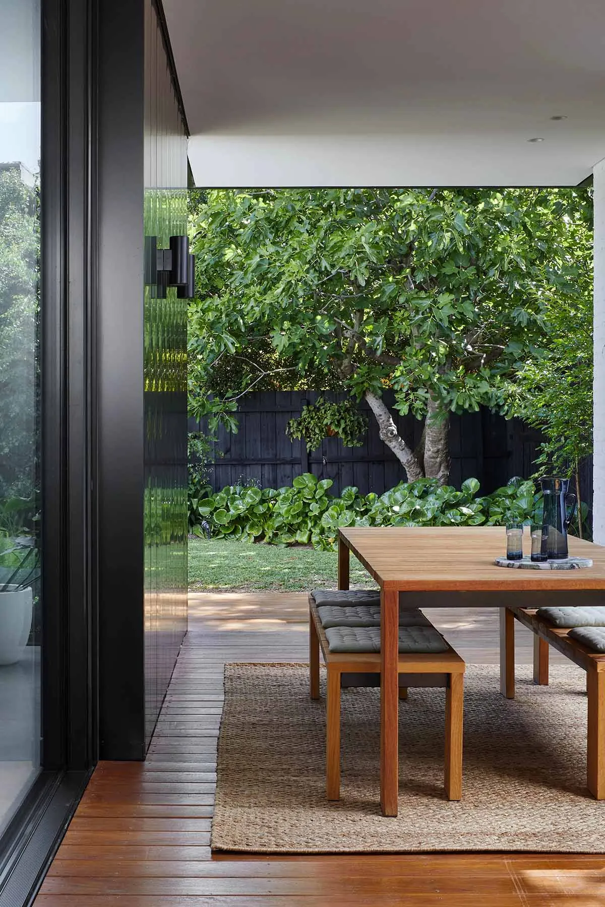 Modern outdoor seating area with wooden table, greenery, and trees