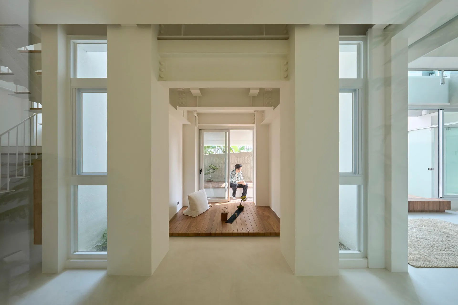 A minimalist interior space with white walls, wood flooring, and a concrete structure.