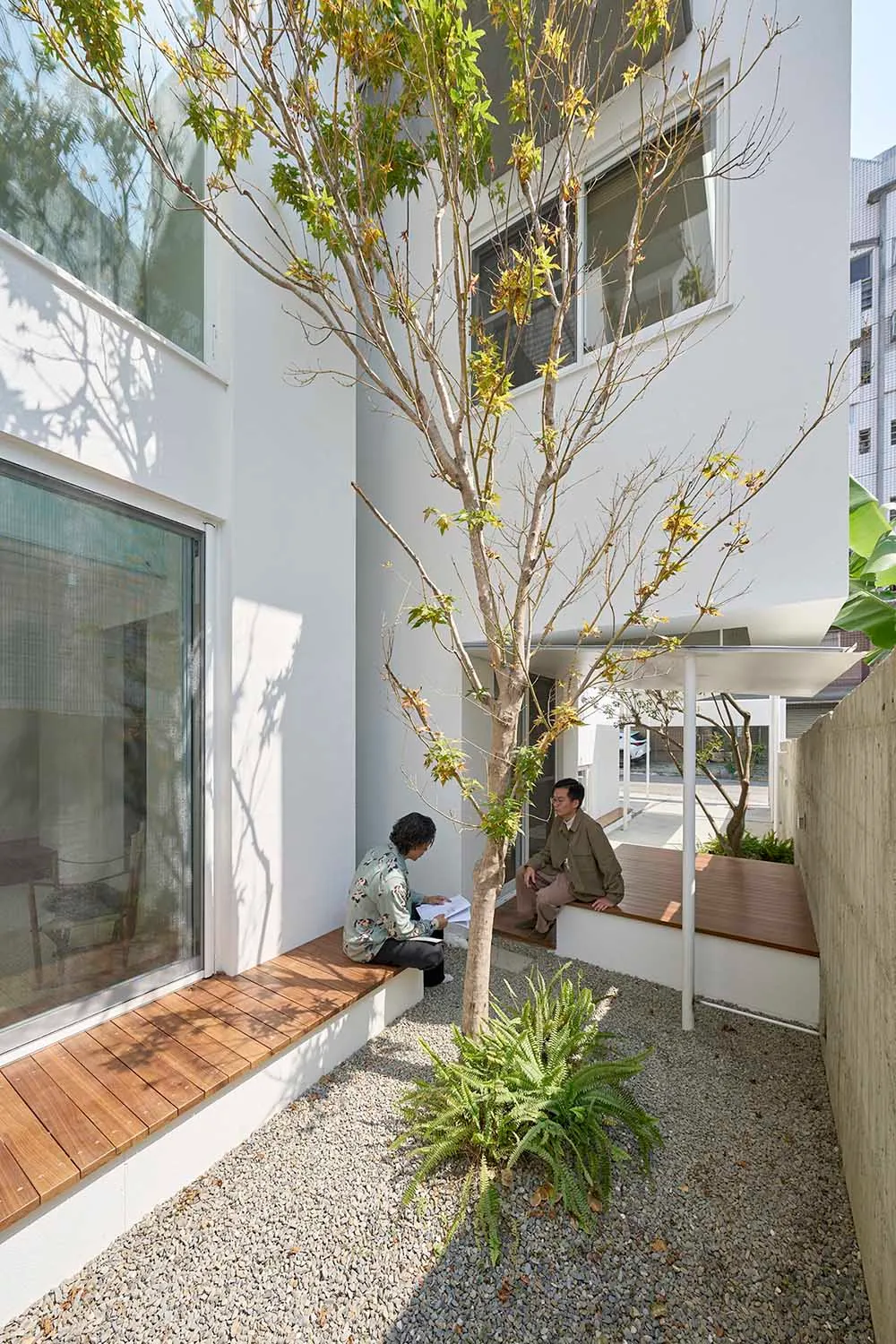 極簡住宅戶外空間，採用混凝土與木質材料，兩人坐在長椅上