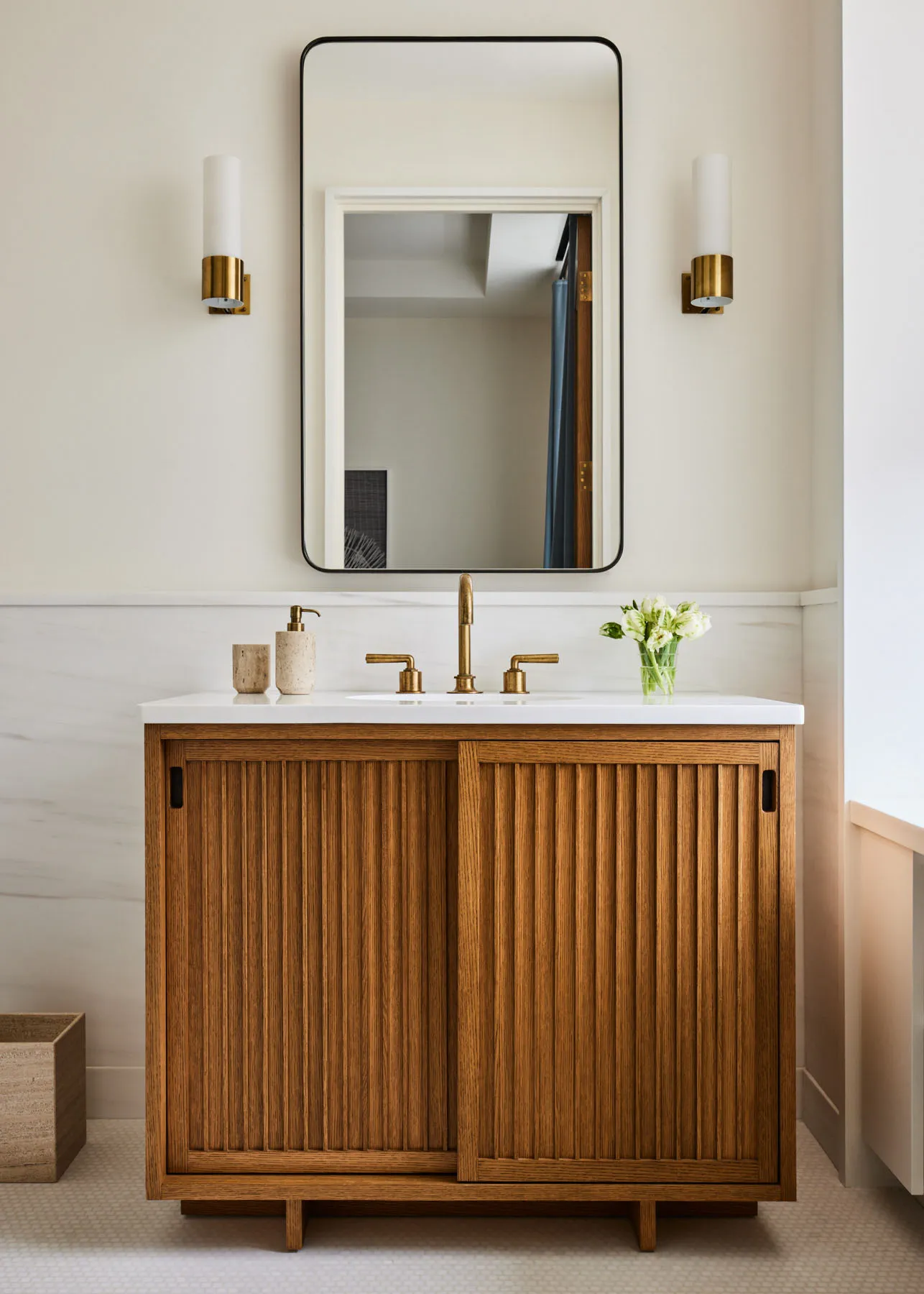 Modern bathroom with a wooden cabinet, white marble countertop, and brass fixtures.