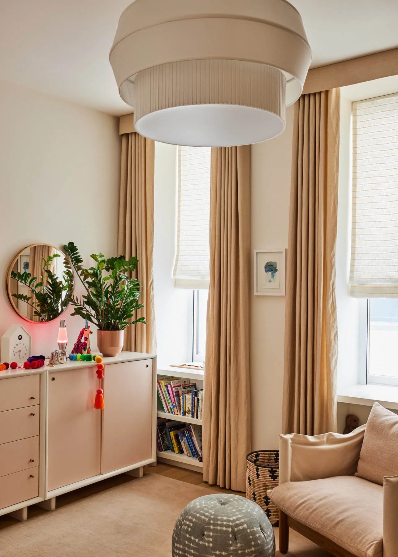 A cozy modern bedroom featuring beige curtains, a plush cushion, a side table, and a window with a white blind.