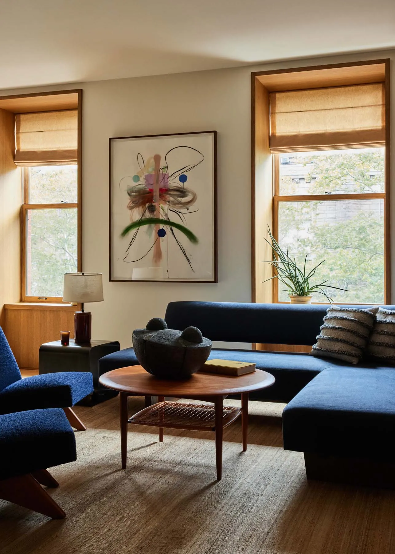 A modern blue sofa in a living room with abstract artwork and potted plant.