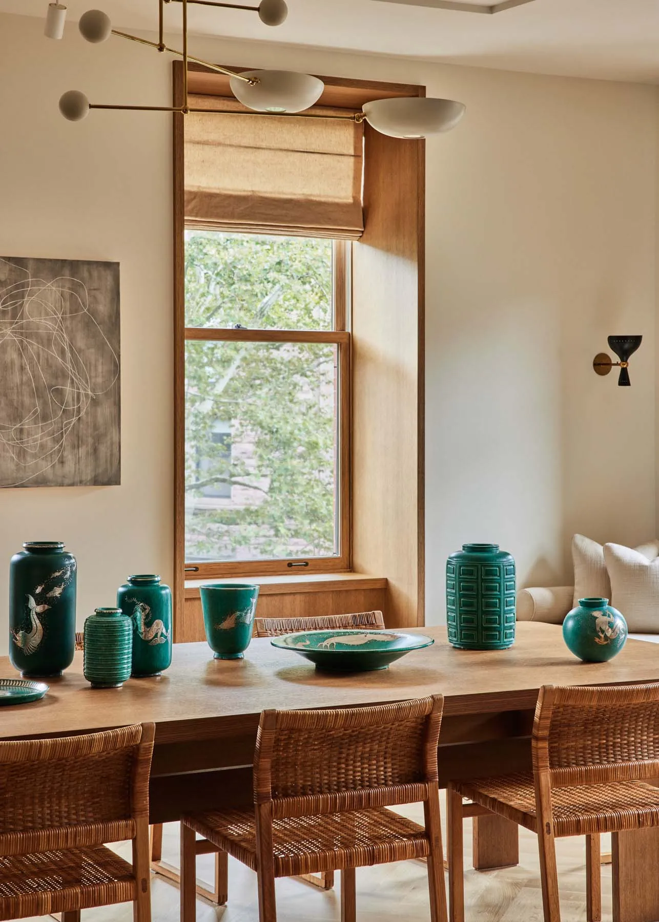 Modern dining room featuring a wooden table and chairs surrounded by turquoise ceramic vases and a large window.