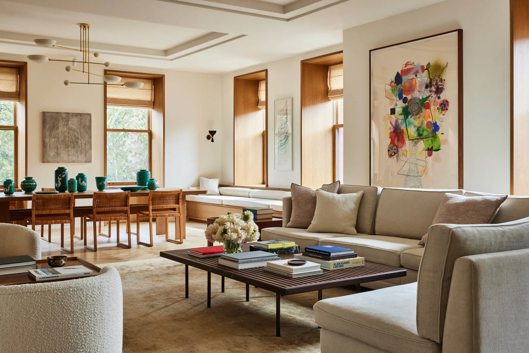 A modern minimalist living room with elegant furniture includes a beige sectional sofa, wooden coffee table, and a few books,