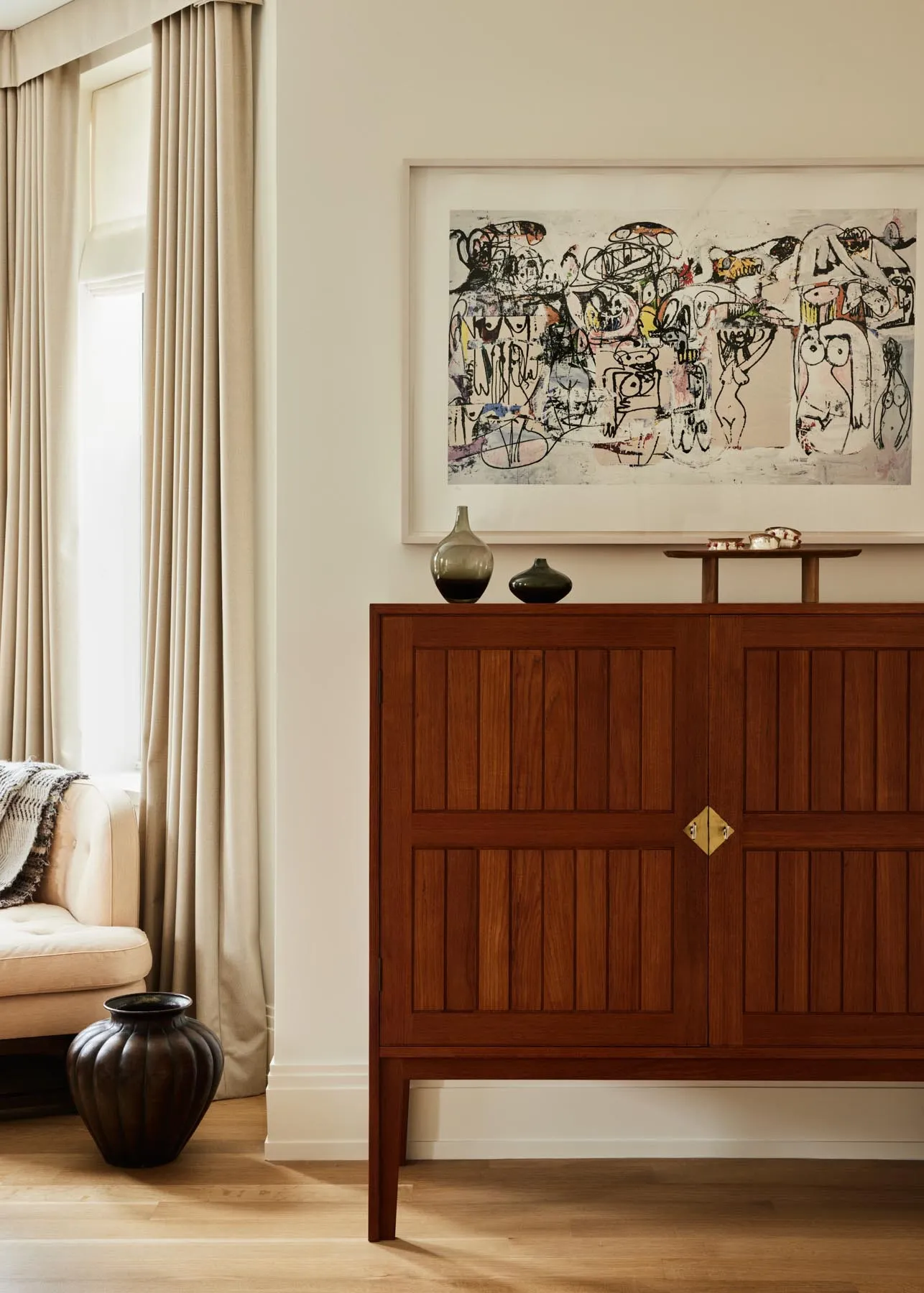 Modern living room featuring a wooden cabinet with artwork on the wall and a comfortable seating area by the window.