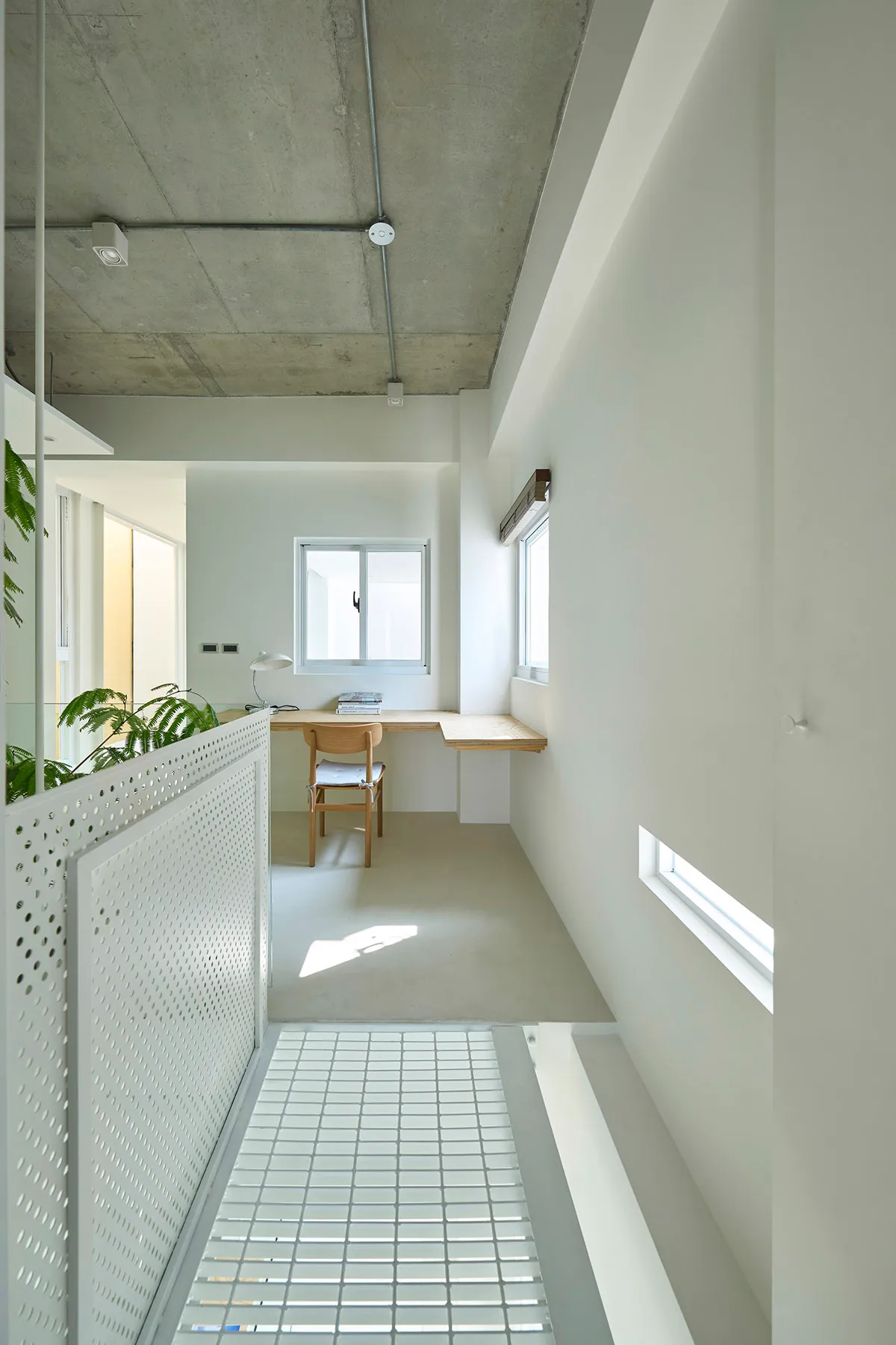 Minimalist office space with concrete floor and walls, featuring a simple wooden desk and chair, and a small window.