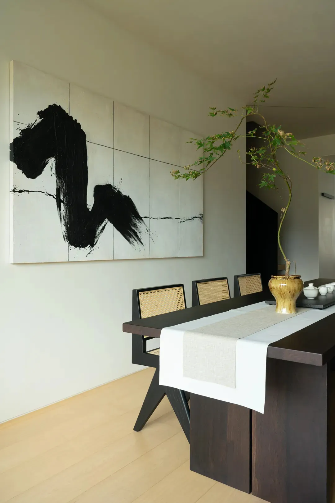 Minimalist dining room featuring wooden furniture and a black and white abstract painting on the wall.