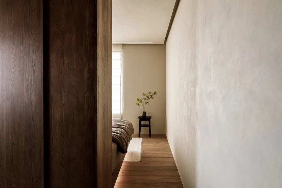 A minimalist bedroom featuring solid wood furniture and a natural plant on a small table.