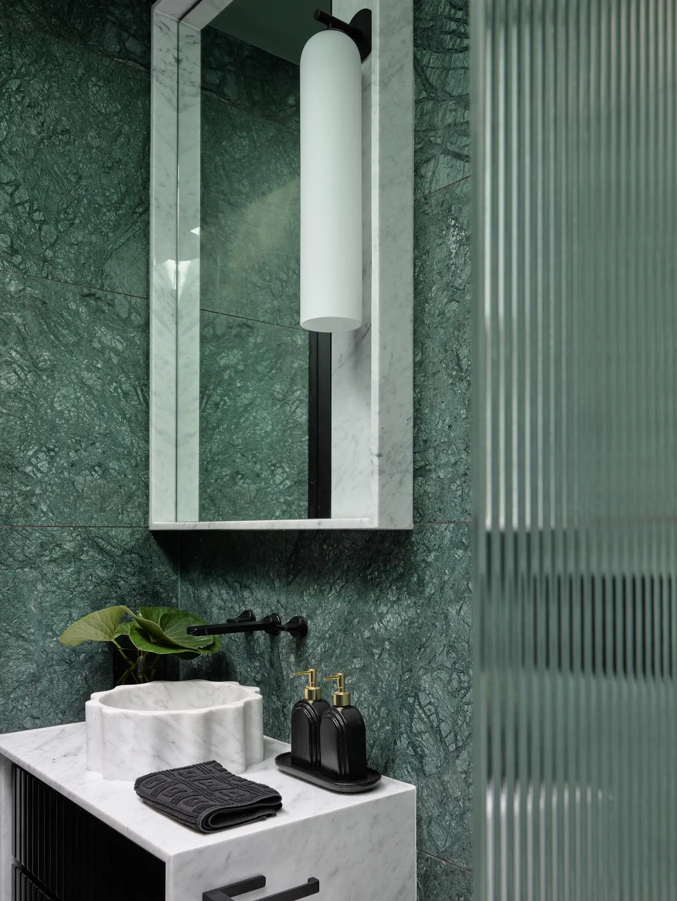 A modern bathroom with green marble walls, a glass shower enclosure, and black and white checkered floor tiles.