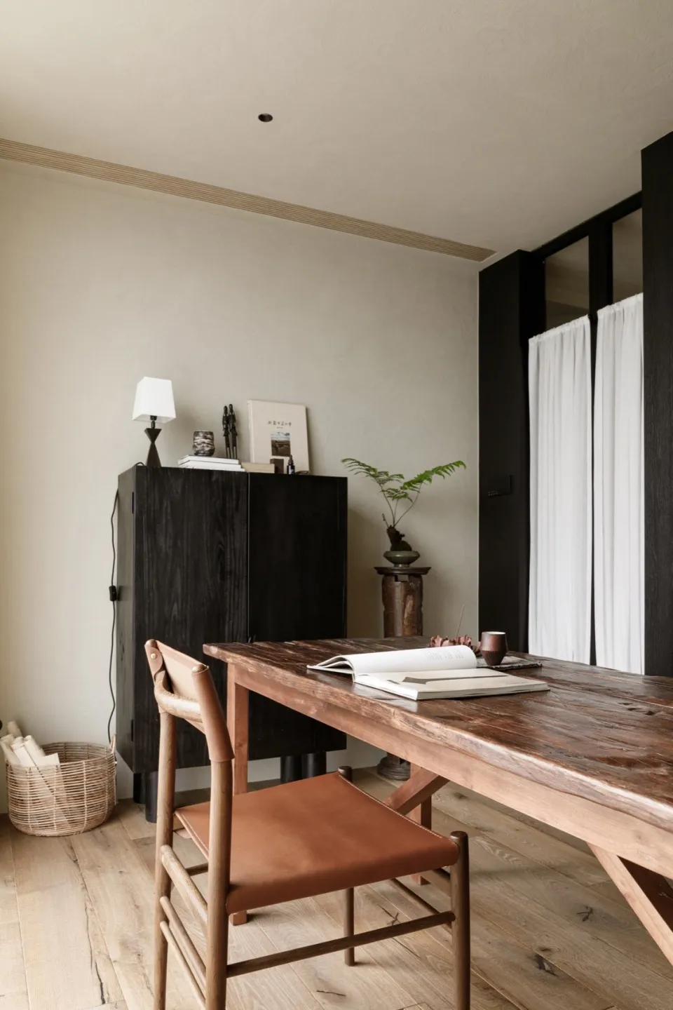 A modern home office featuring a wooden table and chair, minimalist decor, and natural lighting.