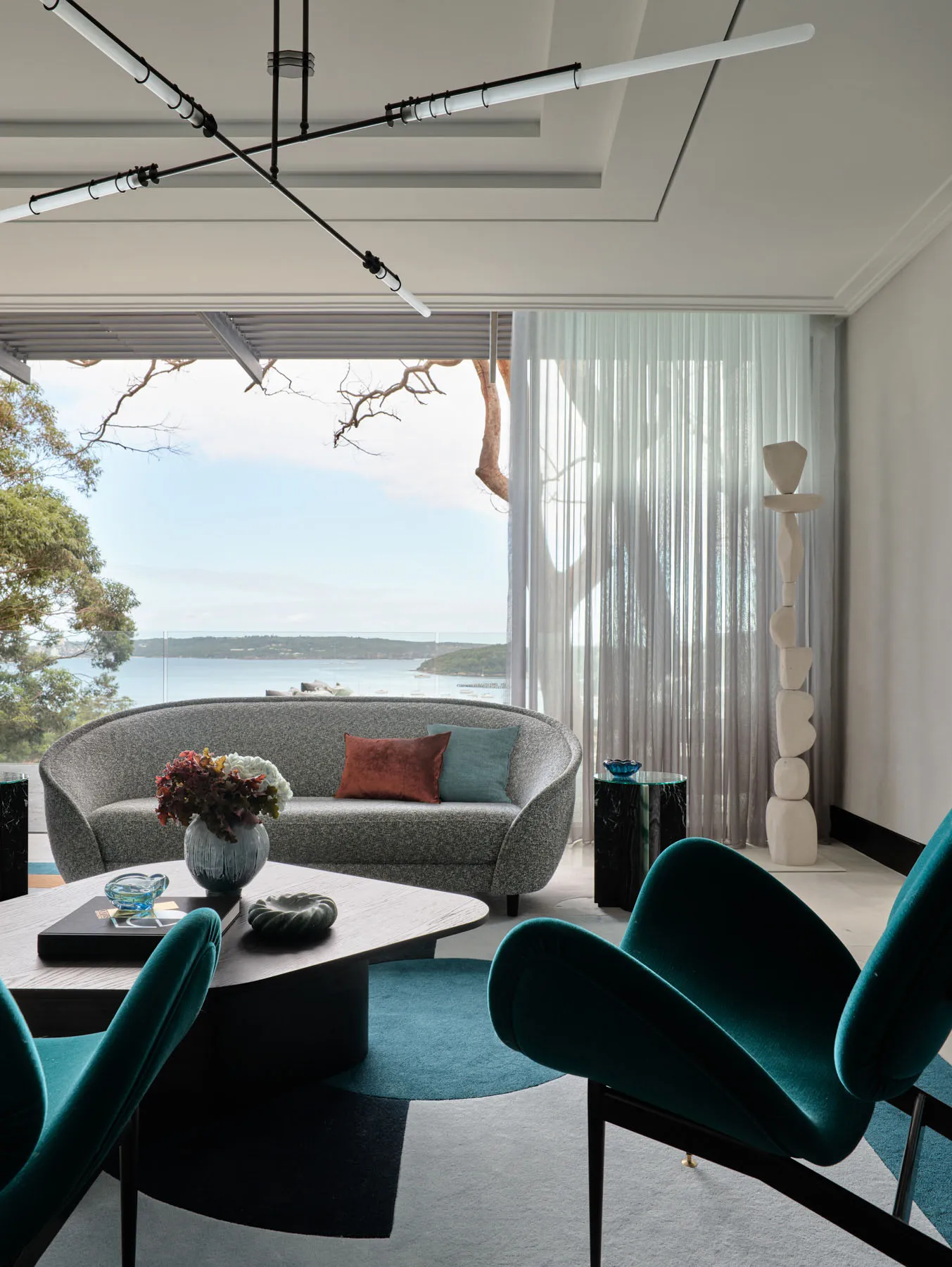 A modern living room features a gray fabric sofa with blue and brown cushions, green velvet armchairs, a coffee table, and a