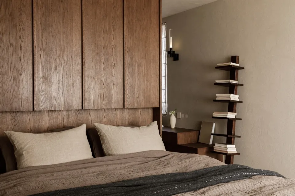 Modern minimalist bedroom featuring a brown bed with wooden headboard, shelves, and books.