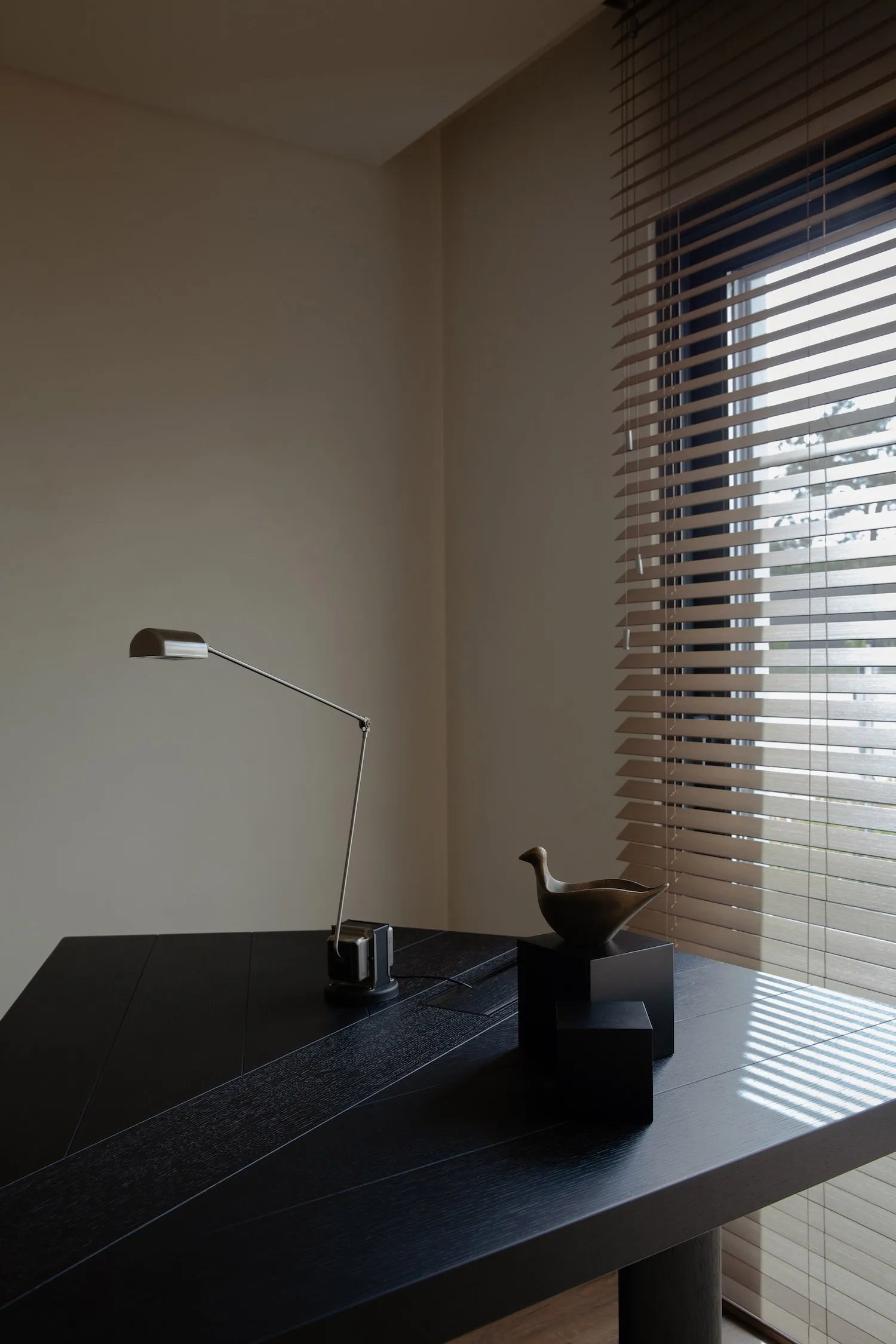 A minimalist office space featuring a black wooden desk with a modern metal lamp and decorative metal bird.