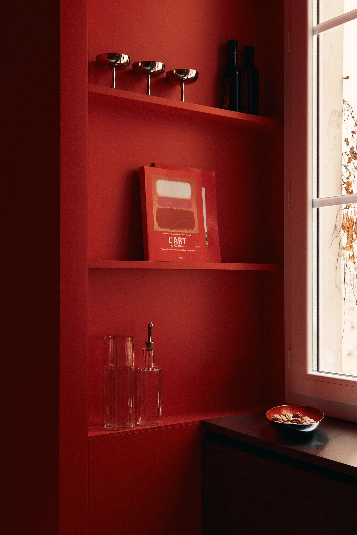A bookshelf with red walls featuring a book with a red cover.