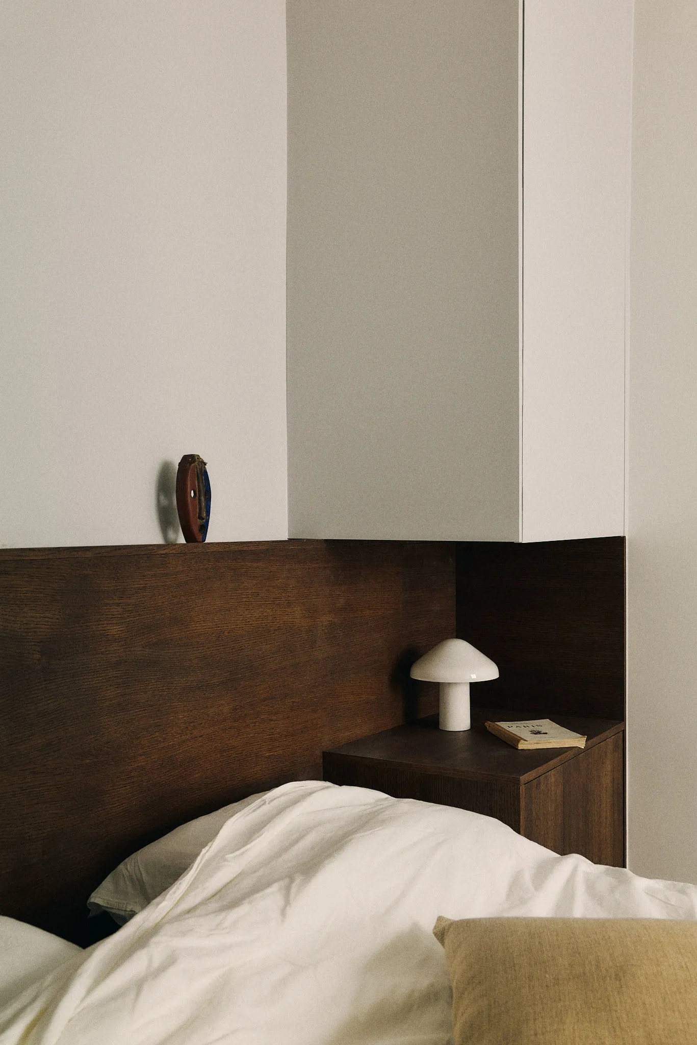 A minimalist bedroom featuring a wooden headboard, ceramic side table, and fabric bedding.