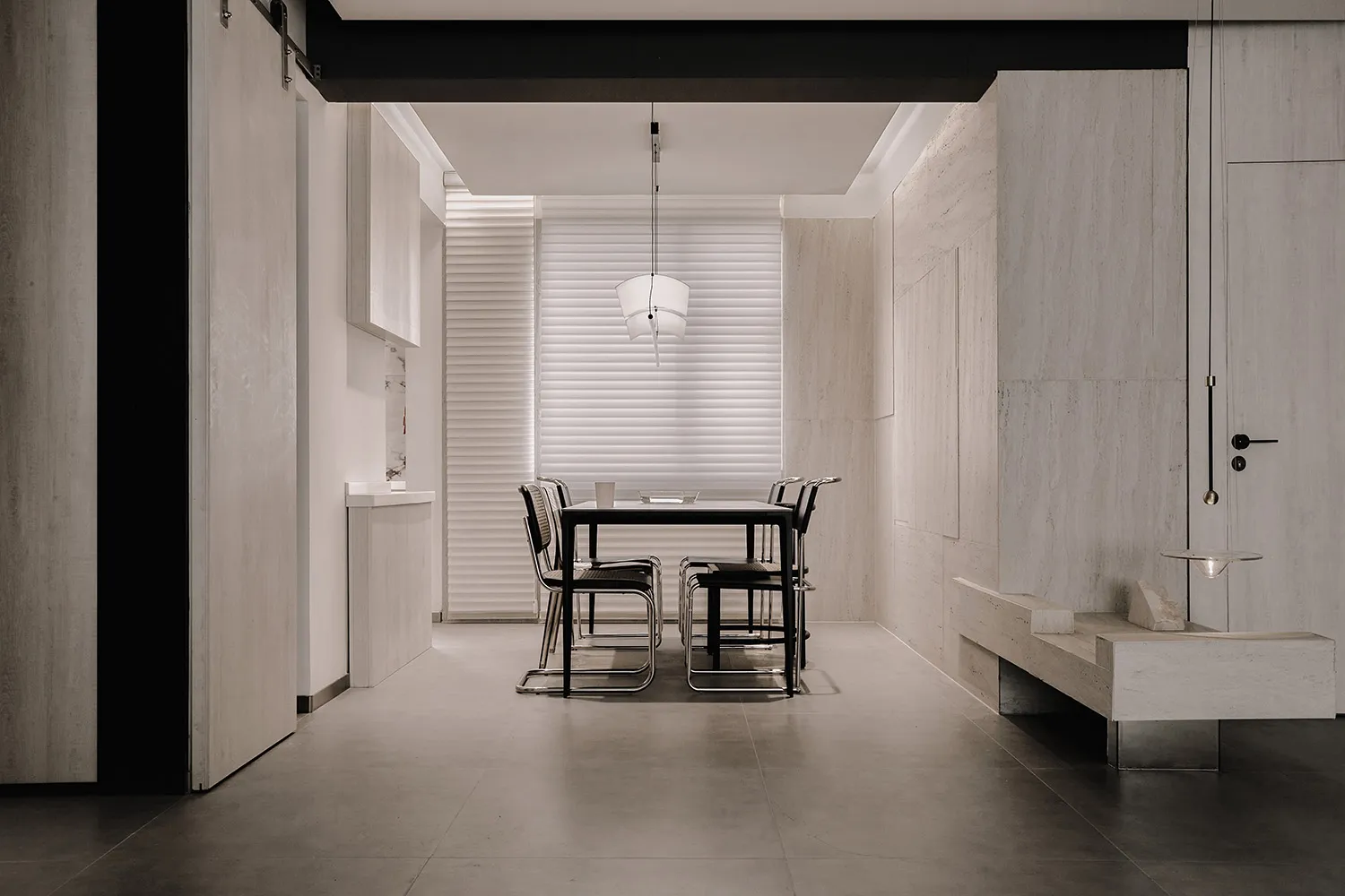 A minimalist dining room featuring concrete walls and a black metal table with chairs.