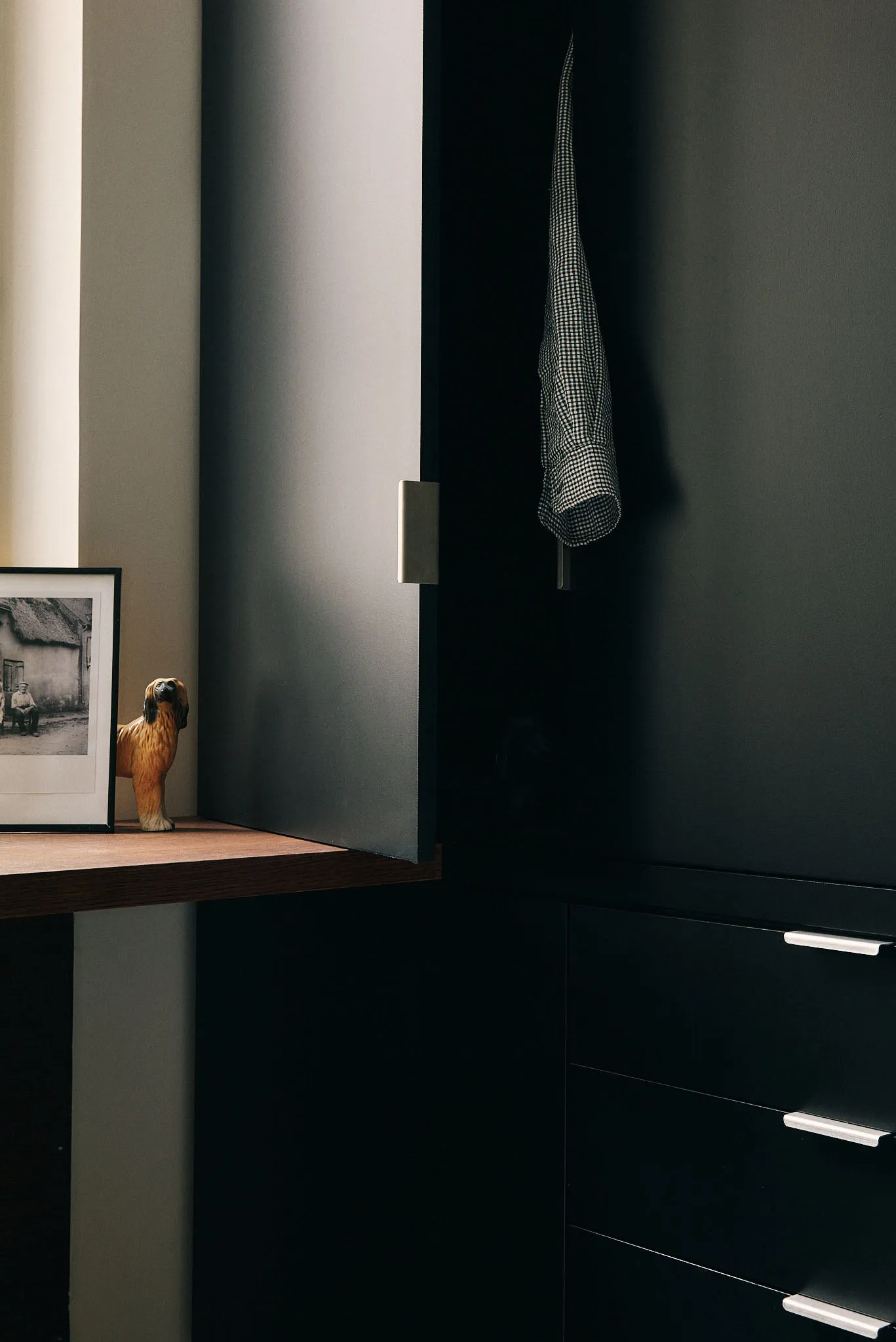 A modern black metallic closet with a checkered shirt hanging inside, a wooden ledge displaying a figurine, and a framed phot