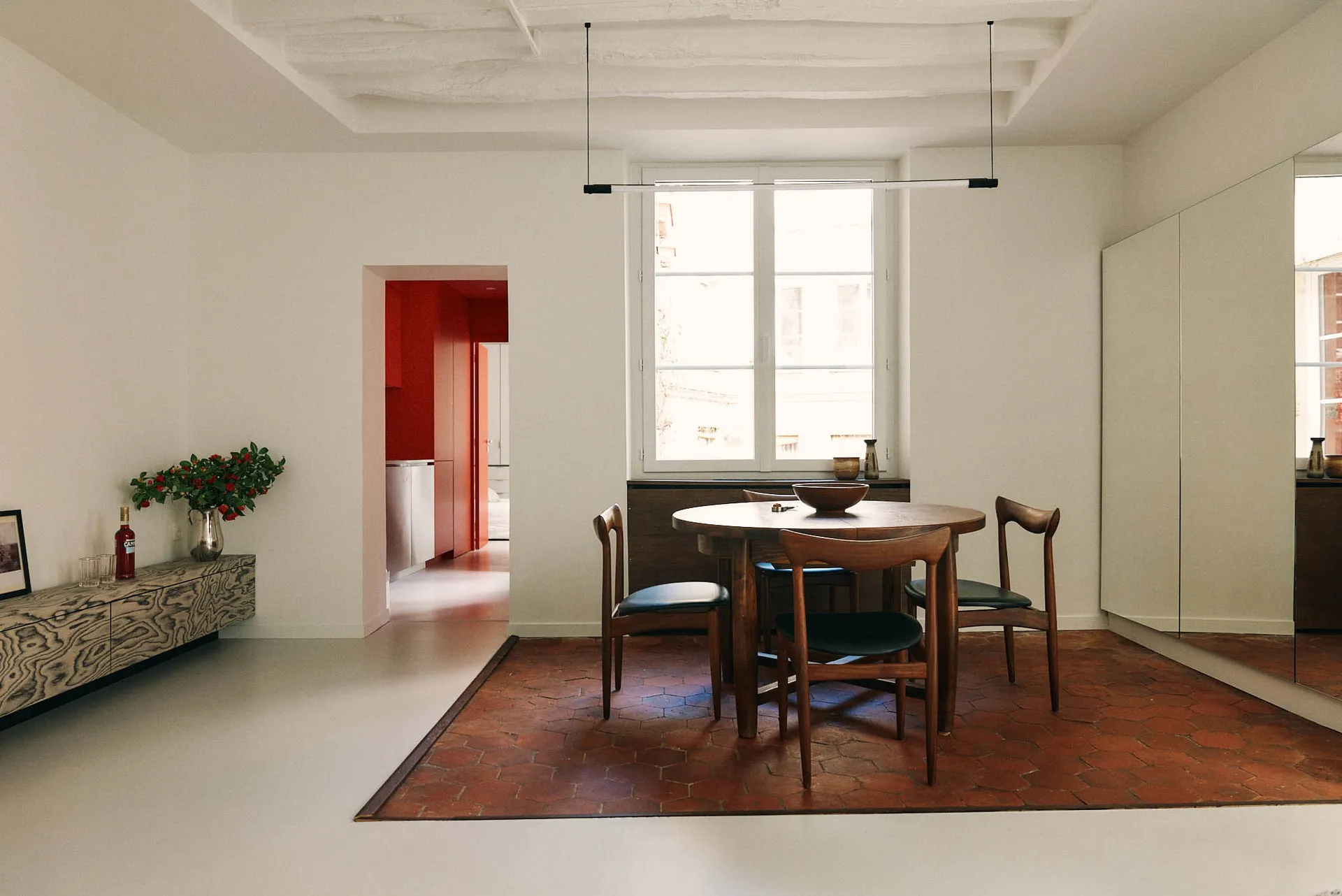 A modern dining room with a round wooden table, black chairs, and a hanging light fixture.