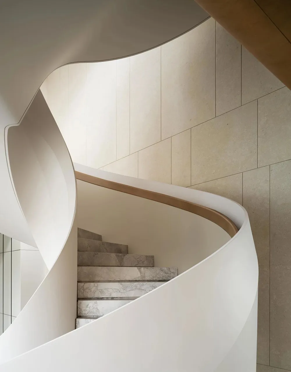 A beautifully curved, modern marble staircase with a white handrail.