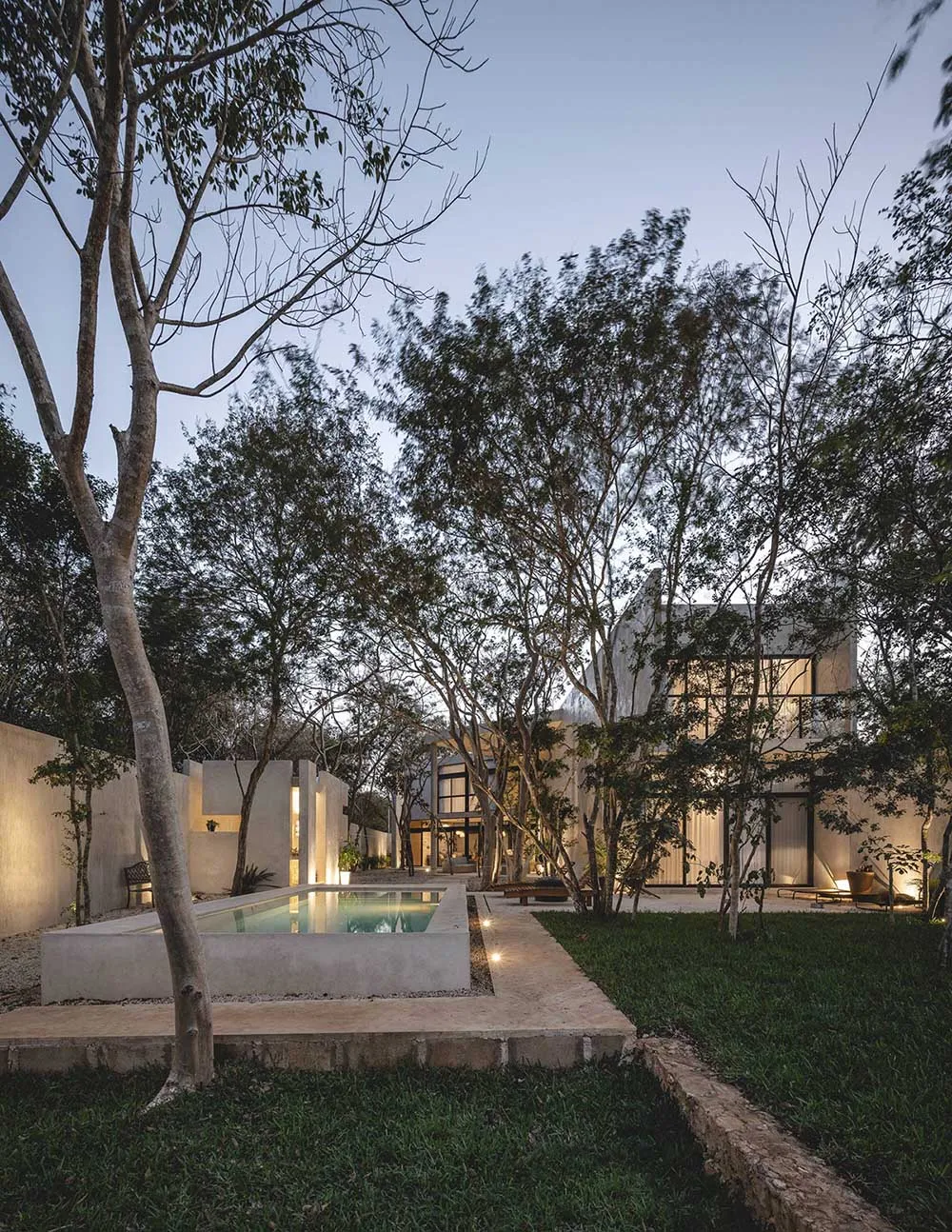 A modern minimalist residential exterior featuring concrete and glass materials surrounded by trees.