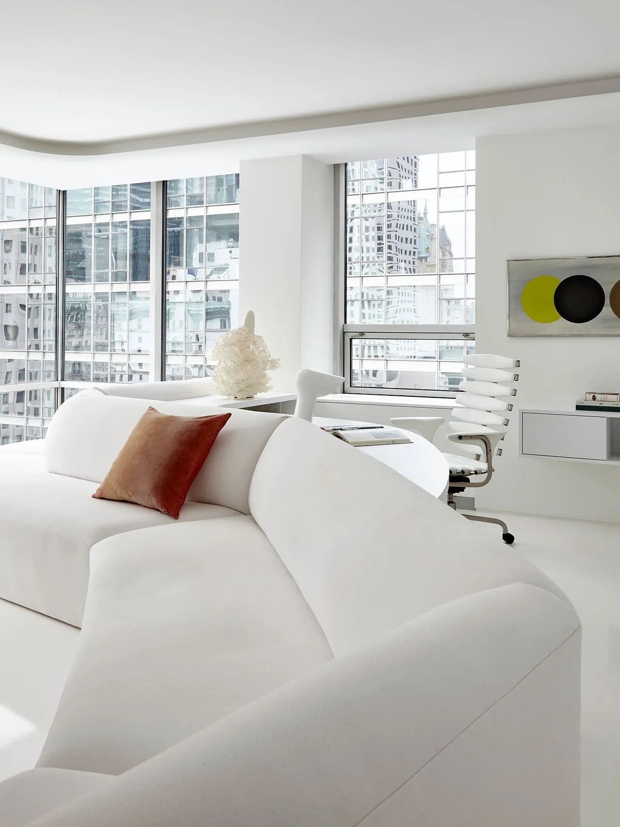 Modern, minimalist living room featuring a white fabric couch with a red throw pillow.