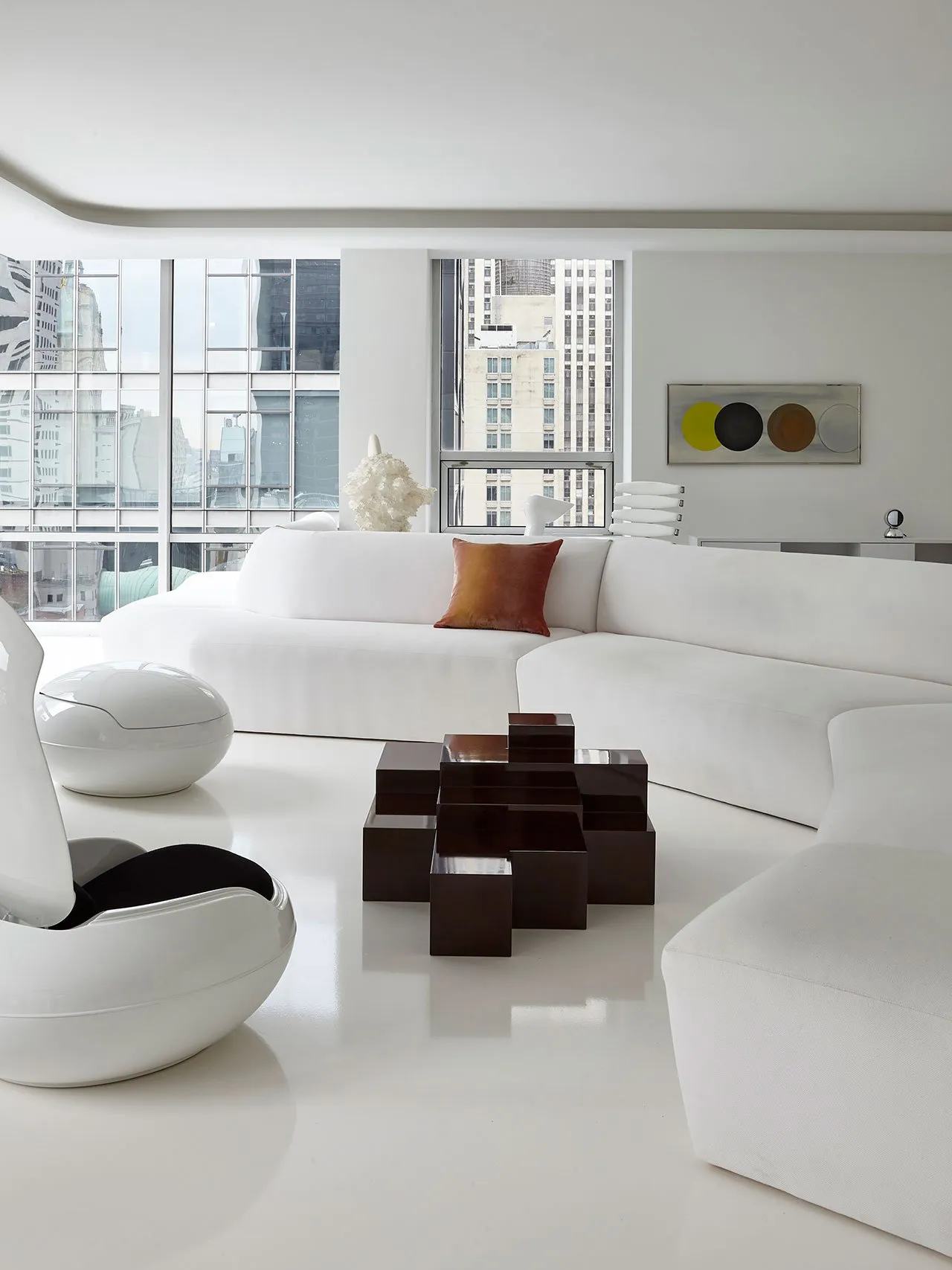 Modern, minimalist white lounge area with fabric seating and geometric coffee table, overlooking urban cityscape.