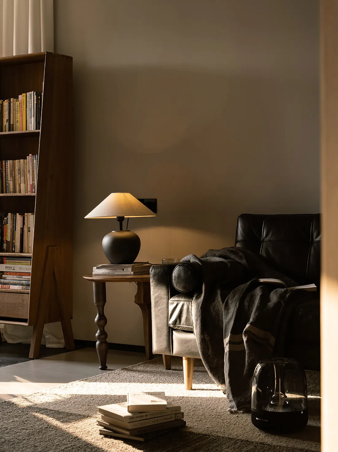 A minimalist living room featuring a wooden armchair, a lamp, and a bookshelf filled with books.