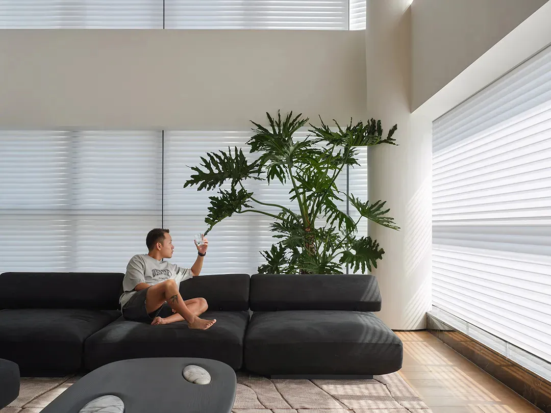 A person sitting on a textured sofa in a modern living room with concrete flooring and large potted plant.