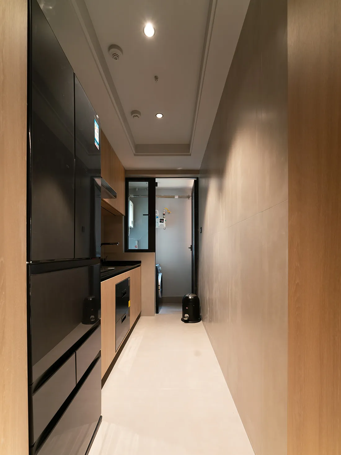 Modern minimalist kitchen with sleek black appliances, wooden cabinets, and white countertops.