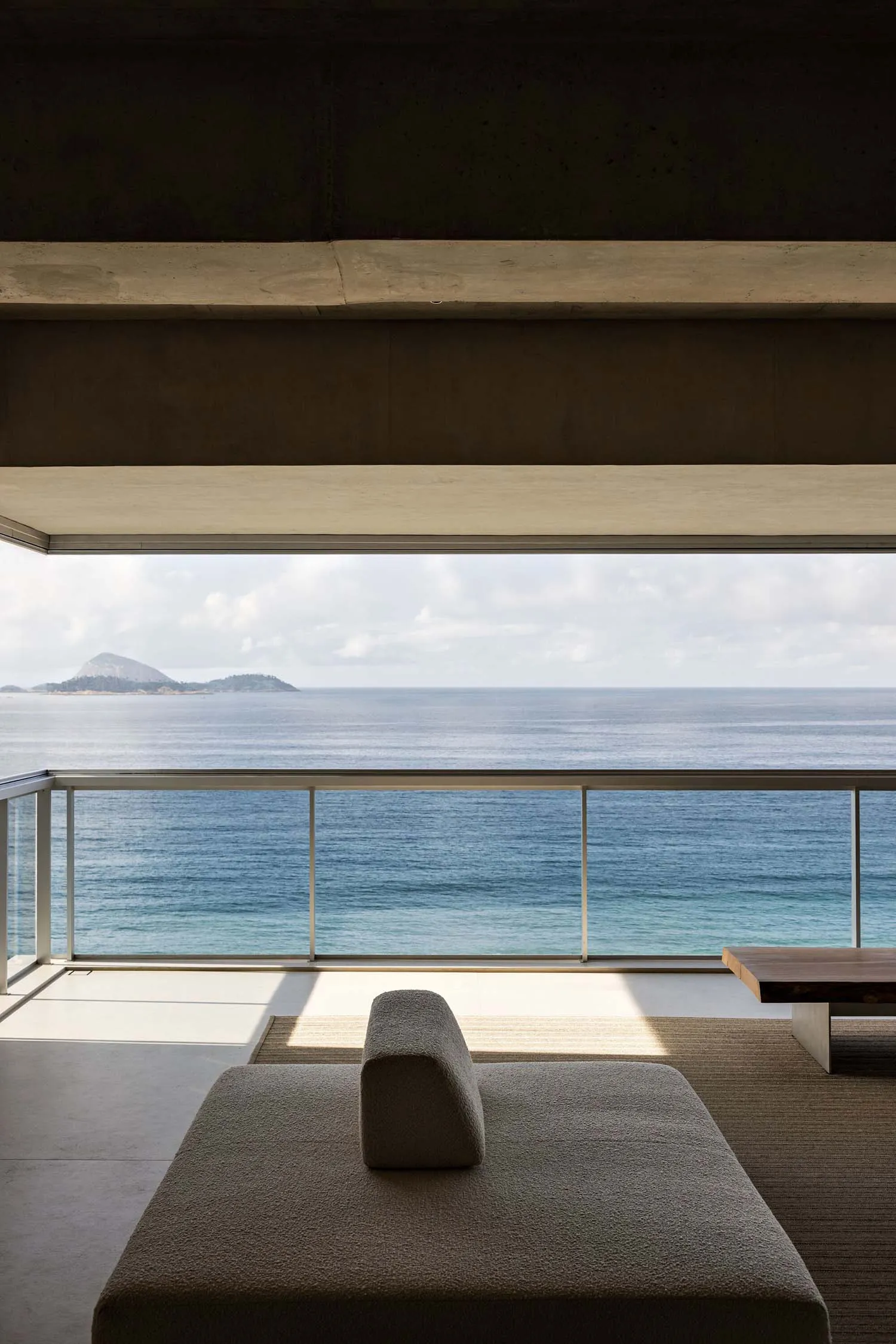A minimalist residential interior featuring concrete and glass materials with a view of the ocean.
