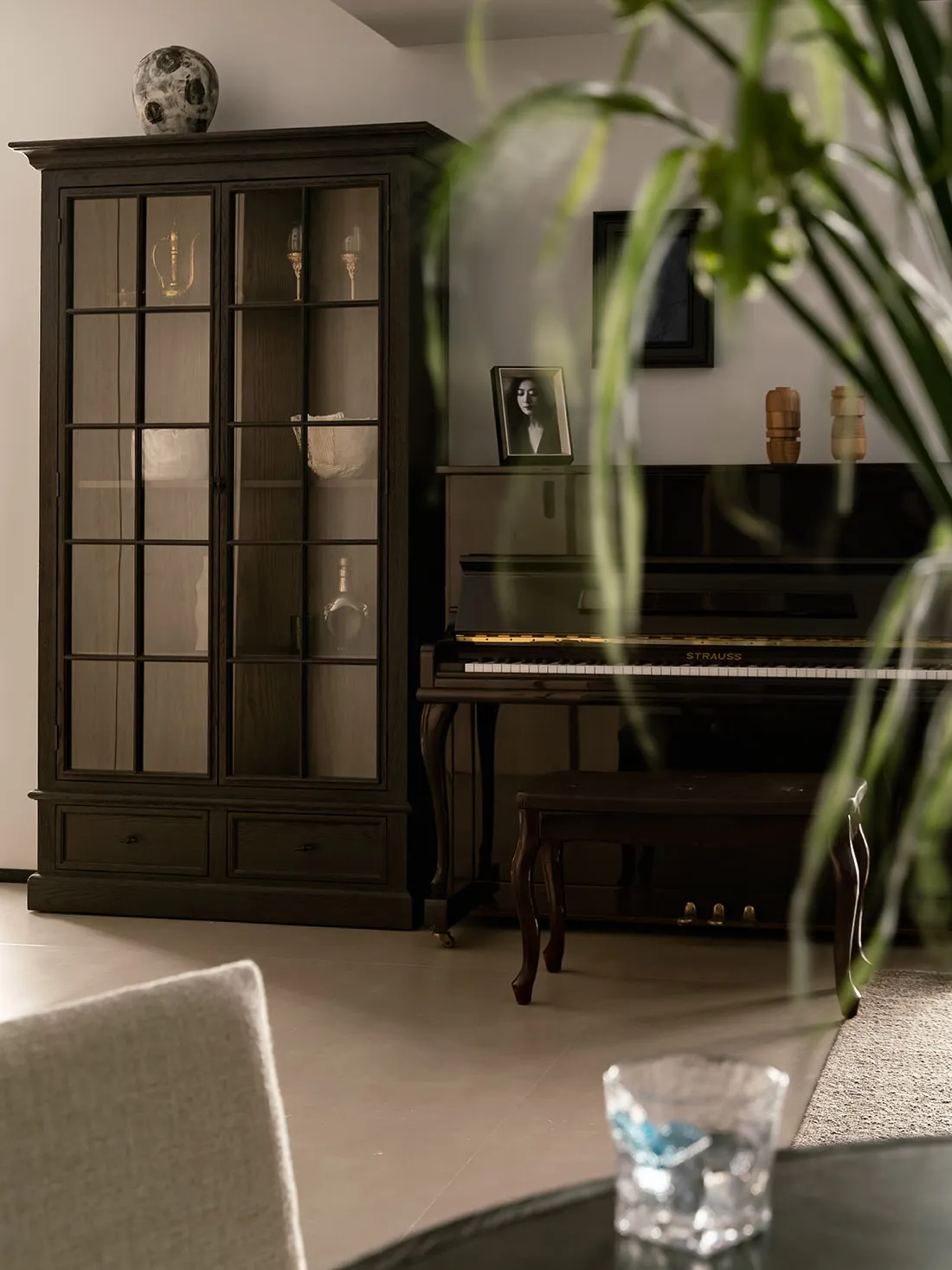 Modern living room featuring a dark wooden console table with glass doors, a glass of water, a potted plant, and a dark uprig