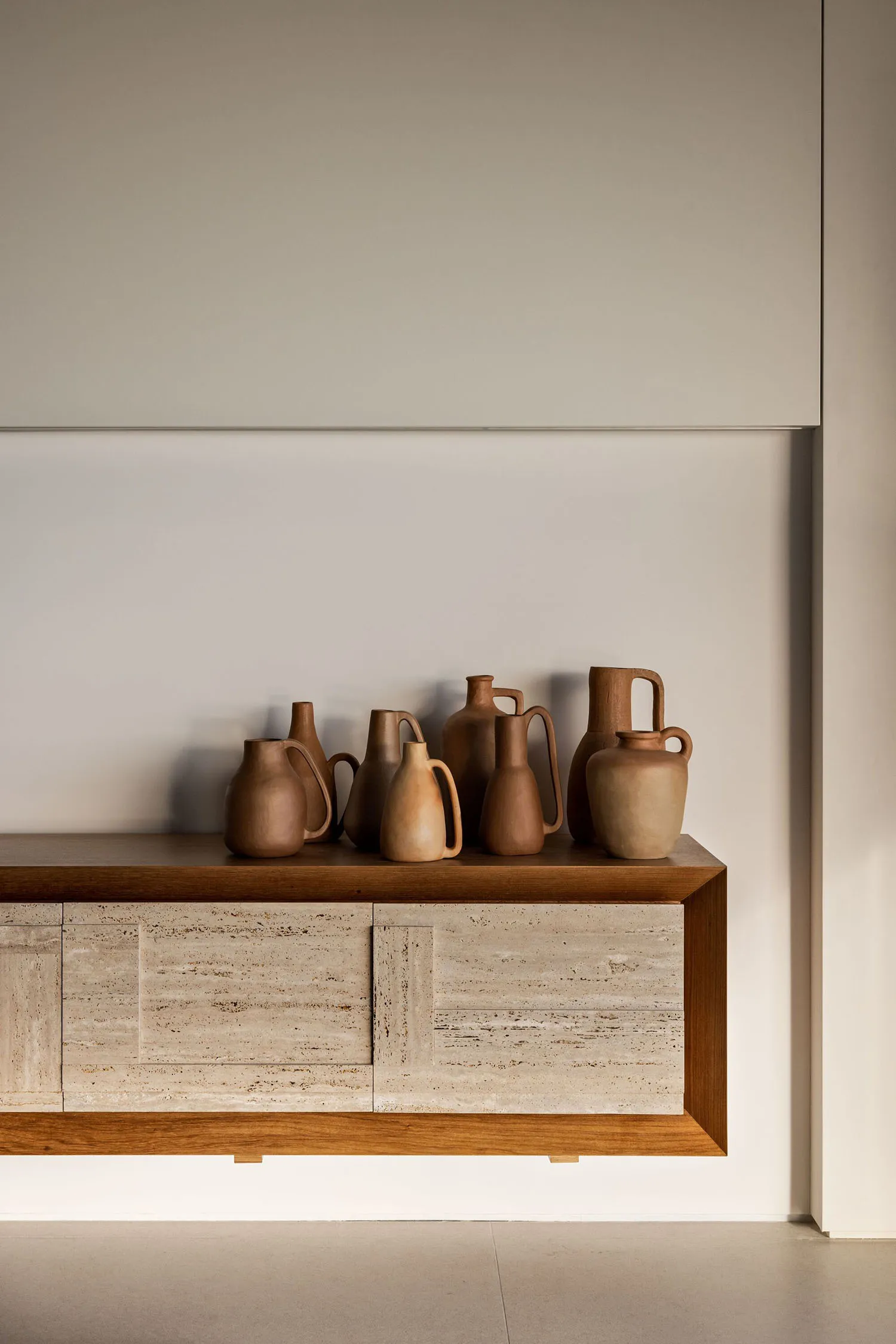 A collection of ceramic vases and jugs displayed on a wooden cabinet against a plain white wall.